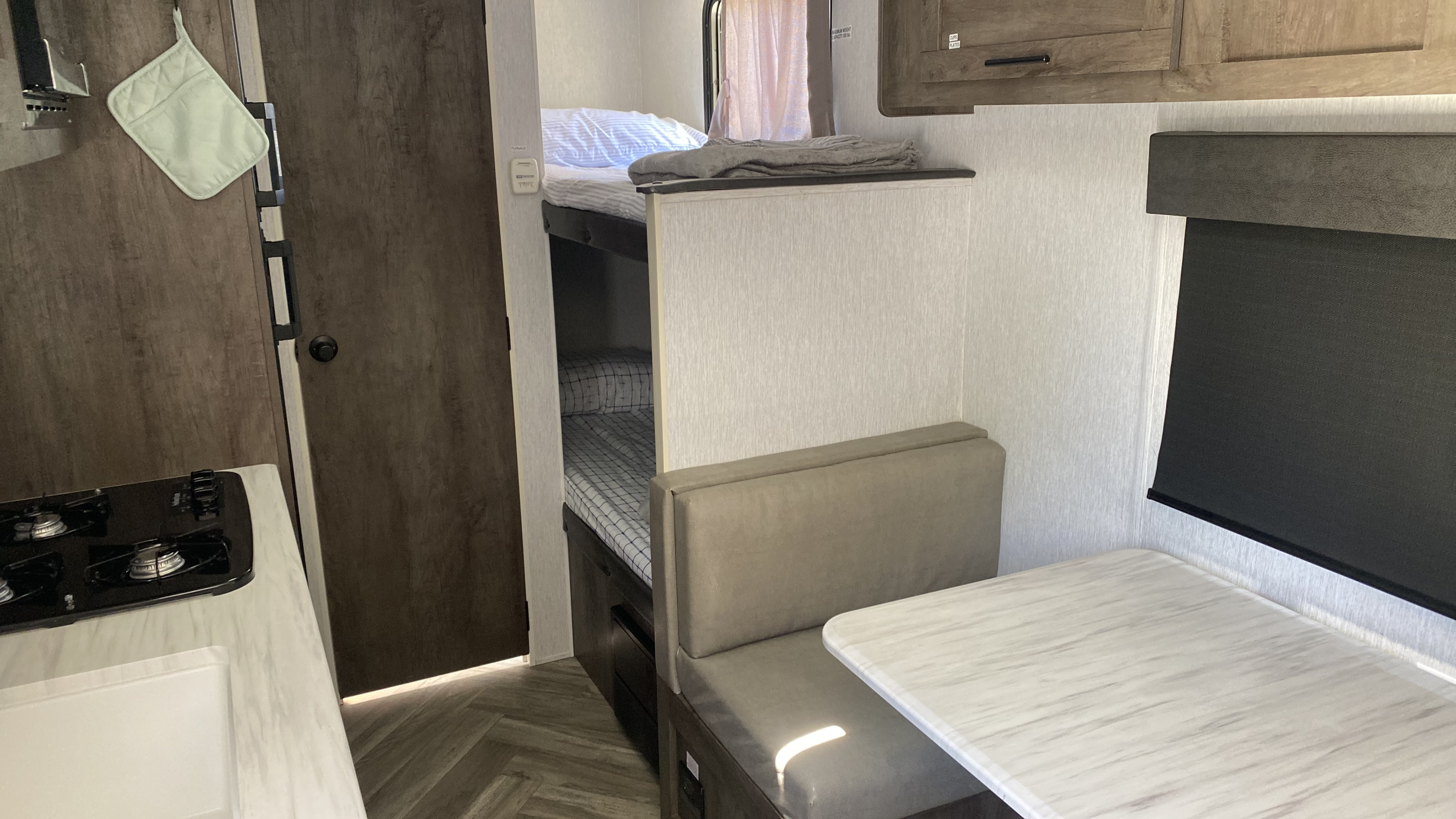 Inside an rv rental: kitchenette with stove, bunk beds with striped bedding, and a dinette table with bench seating.. Forest River EVO 17BHS 2022