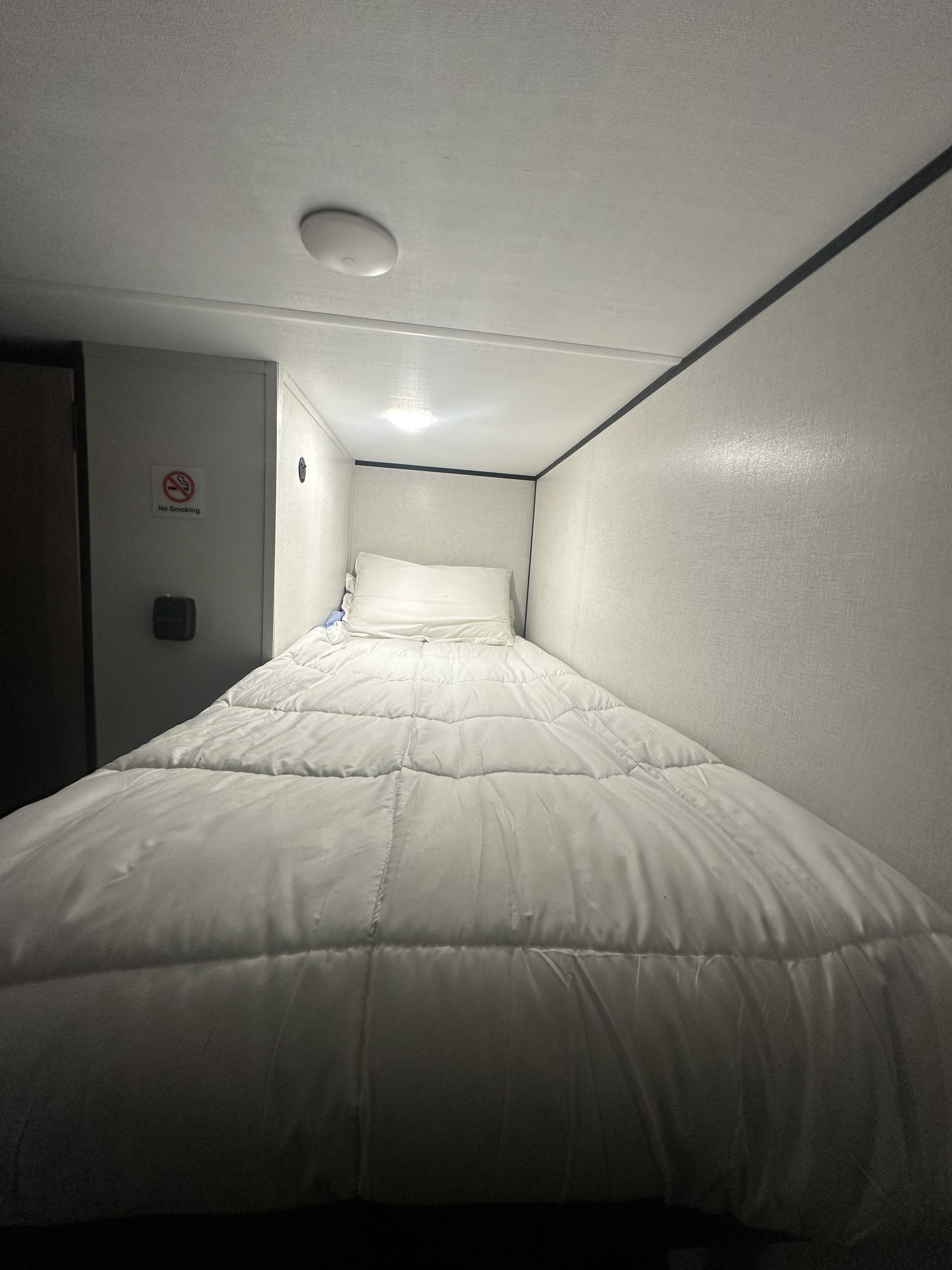 Cozy RV rental bunk bed: narrow sleeping area with white bedding, light walls, and a clear "No Smoking" sign.. Keystone CM17BX26 2026
