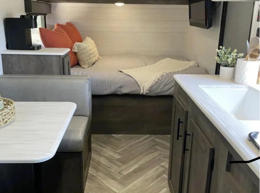 Comfortable RV rental interior featuring a bed with pillows, a dinette, and a compact kitchen area with a sink and coffee maker.. Forest River EVO 17BHS 2022