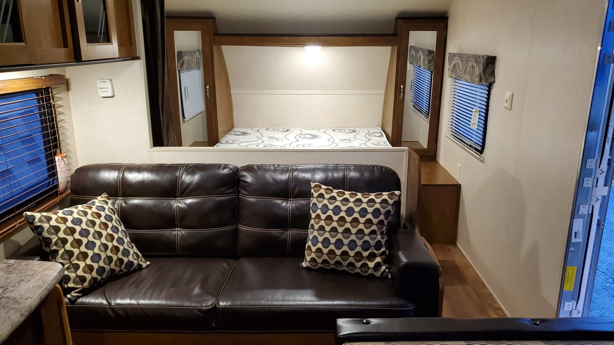 RV rental interior: cozy living space with a brown leather sofa, patterned pillows, and a bed ready for guests.. Forest River Wildwood X-Lite 2018
