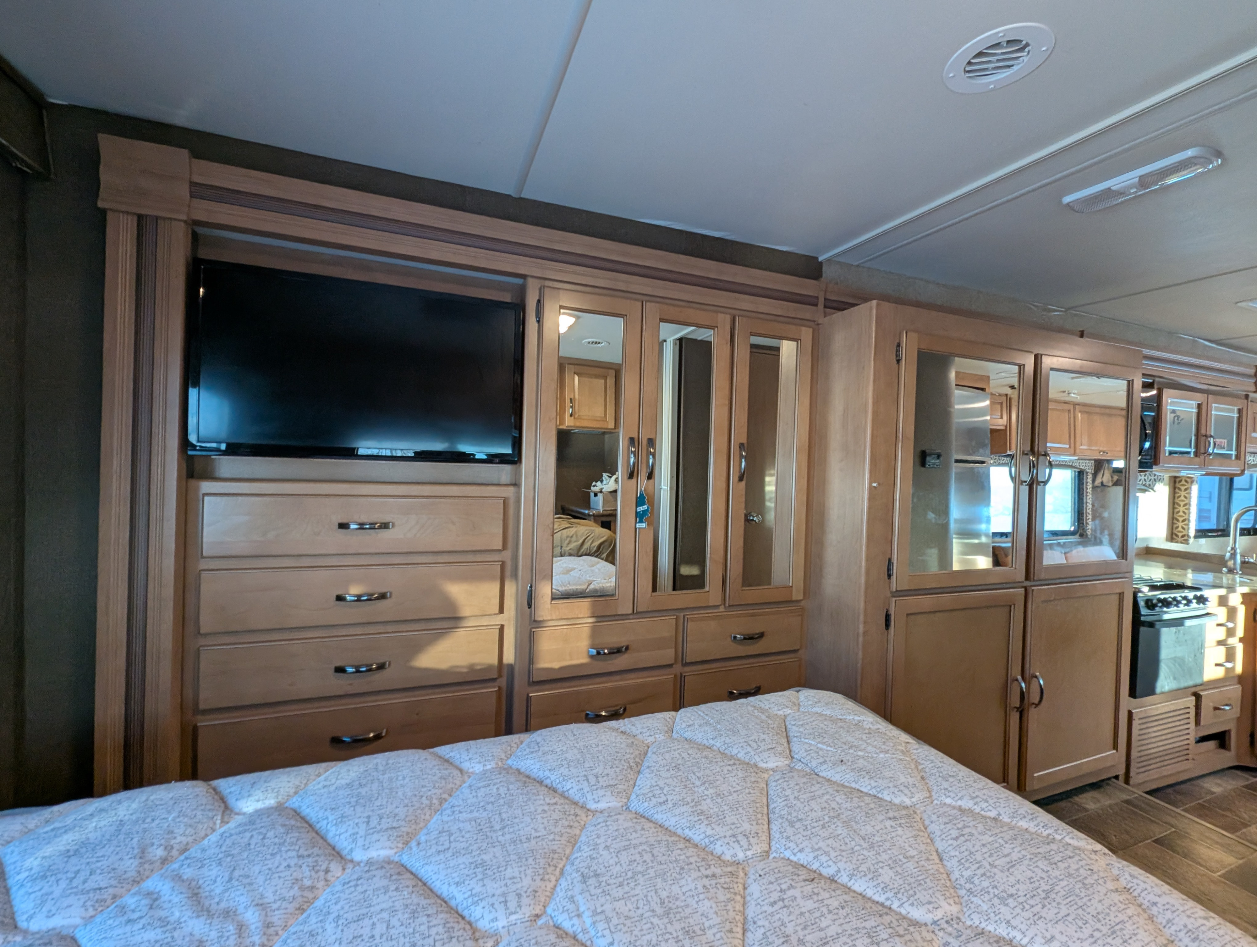 RV rental bedroom: a comfortable bed, TV, drawers, and mirrored closets. Part of the kitchen is visible in the background.. Thor Four Winds 2016