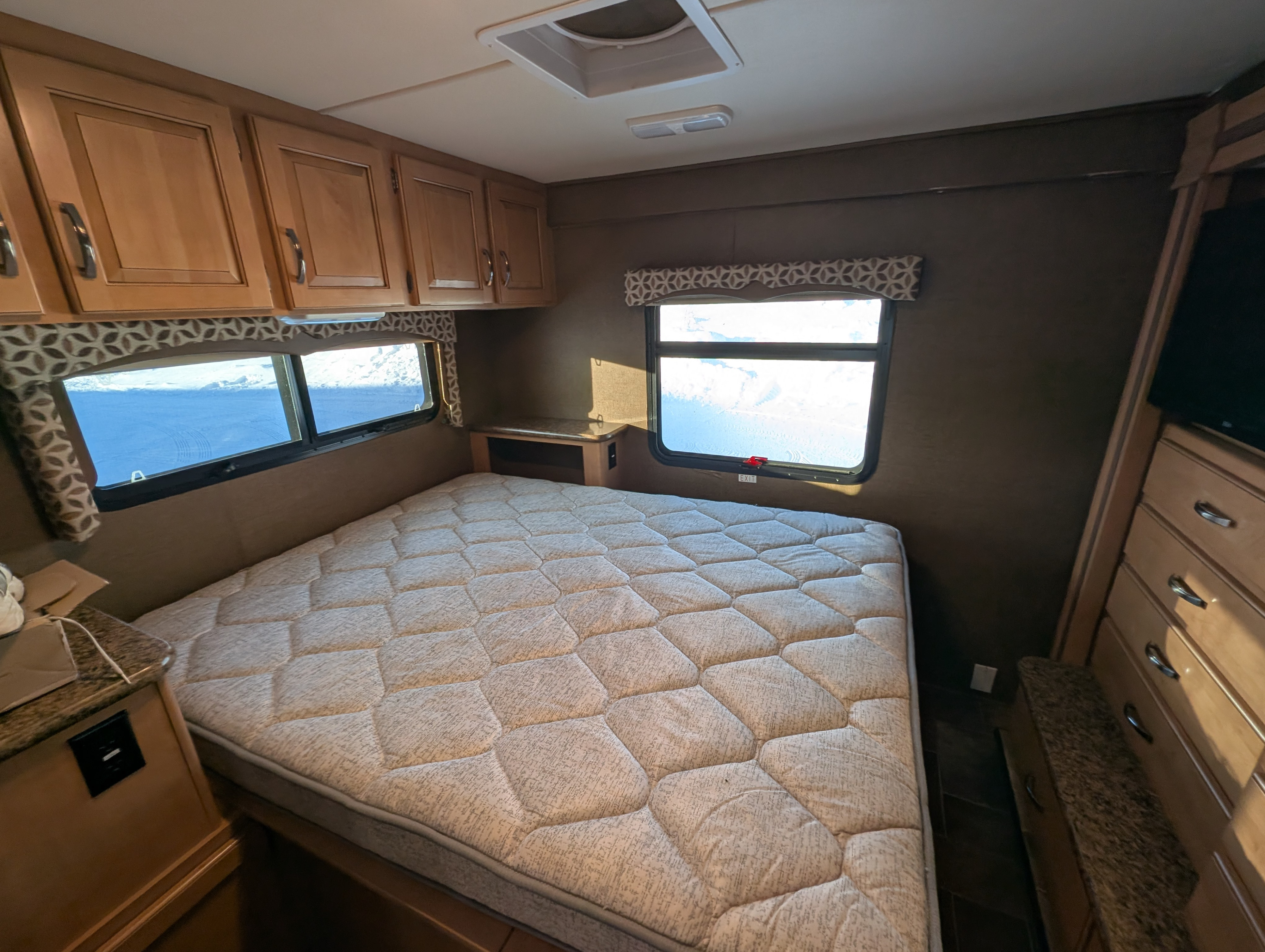 Spacious RV rental bedroom featuring a comfortable bed, wood cabinets, and bright windows with a winter view.. Thor Four Winds 2016