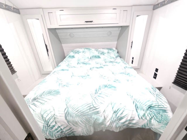 Modern RV rental bedroom. Bright interior with a bed, tropical palm leaf duvet, overhead storage, and side compartments.. Forest River Salem 2022