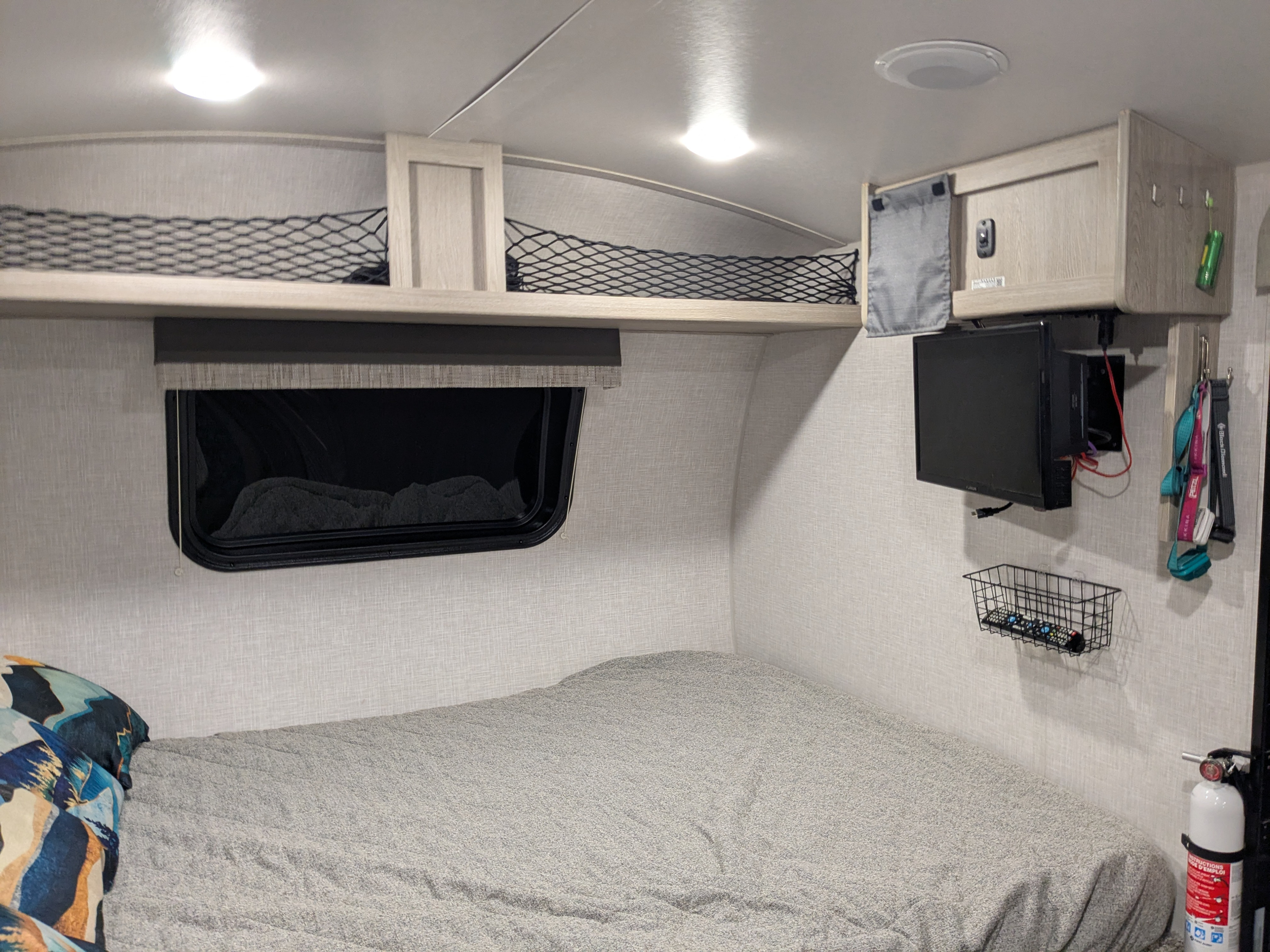 Cozy rv rental bedroom: bed, window, overhead nets, wall-mounted TV, cabinet, and a fire extinguisher for safety.. Forest River Flagstaff E-Pro 2022