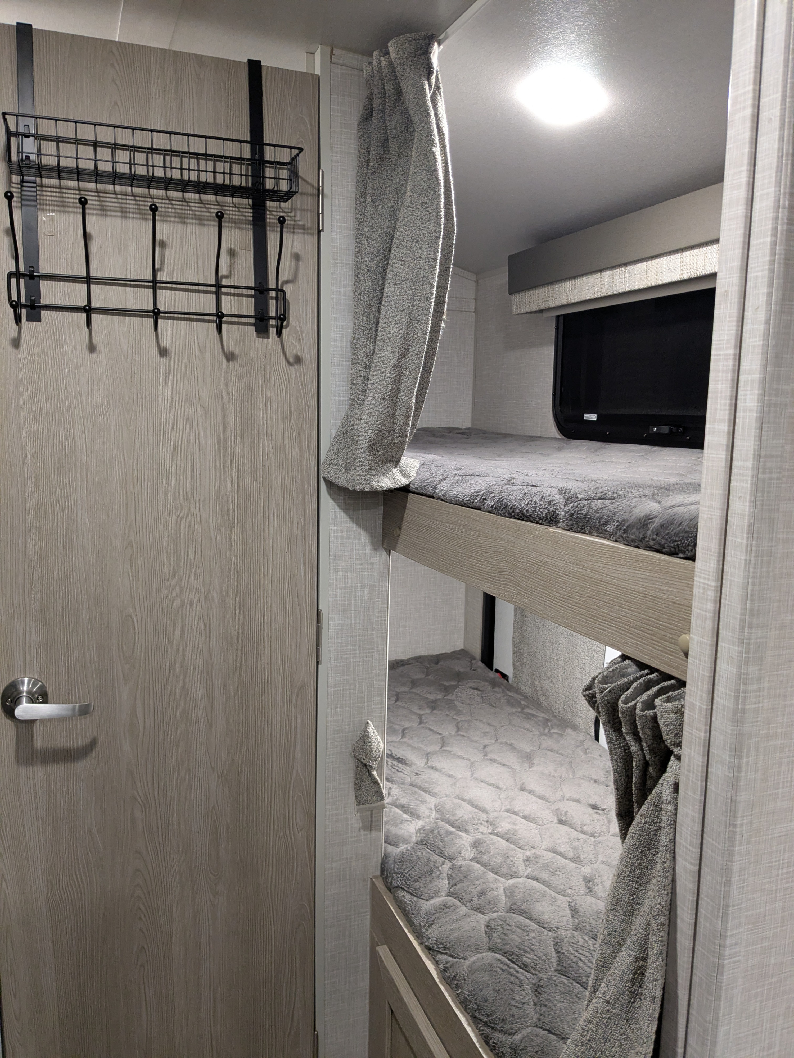 Inside an RV rental: cozy bunk beds with grey bedding, privacy curtains, and a handy over-door rack.. Forest River Flagstaff E-Pro 2022