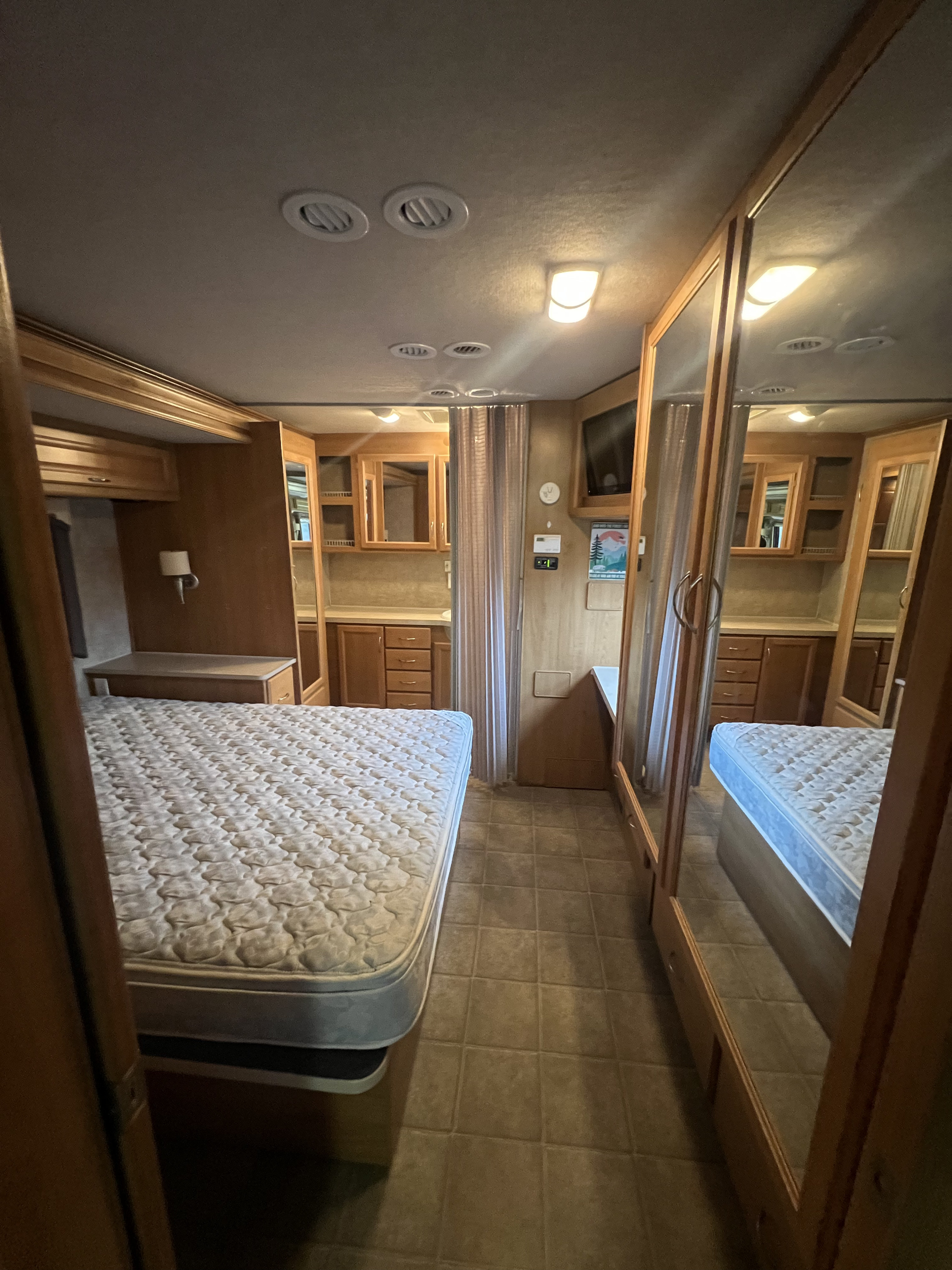 RV rental bedroom featuring a spacious bed, mirrored closets, and wood-paneled cabinetry; ideal for travel accommodations.. Fleetwood Bounder 2008