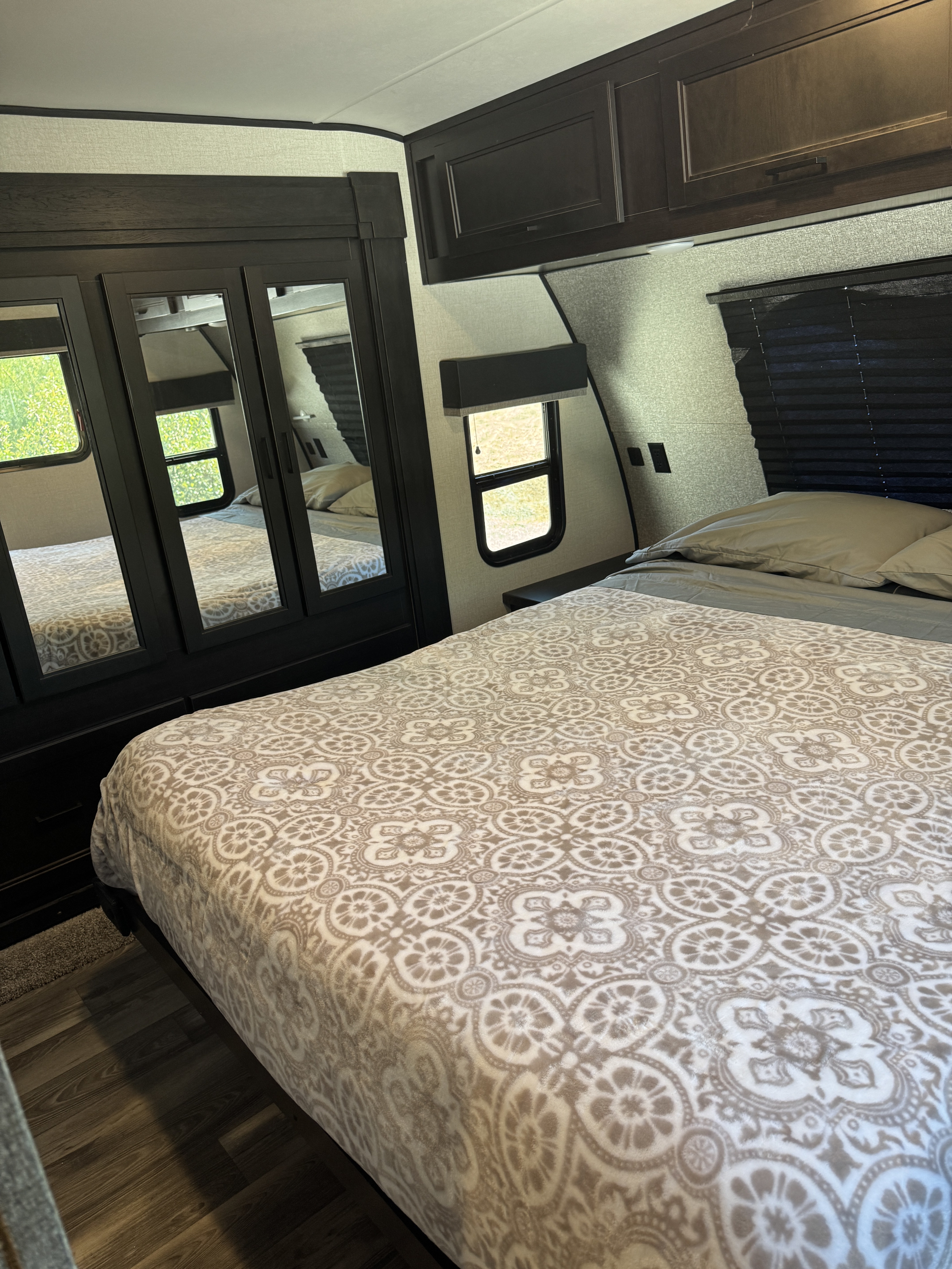 Cozy RV rental bedroom featuring a patterned bedspread, mirrored wardrobe, and dark wood overhead cabinets.. Highland Ridge RV Mesa Ridge 2022