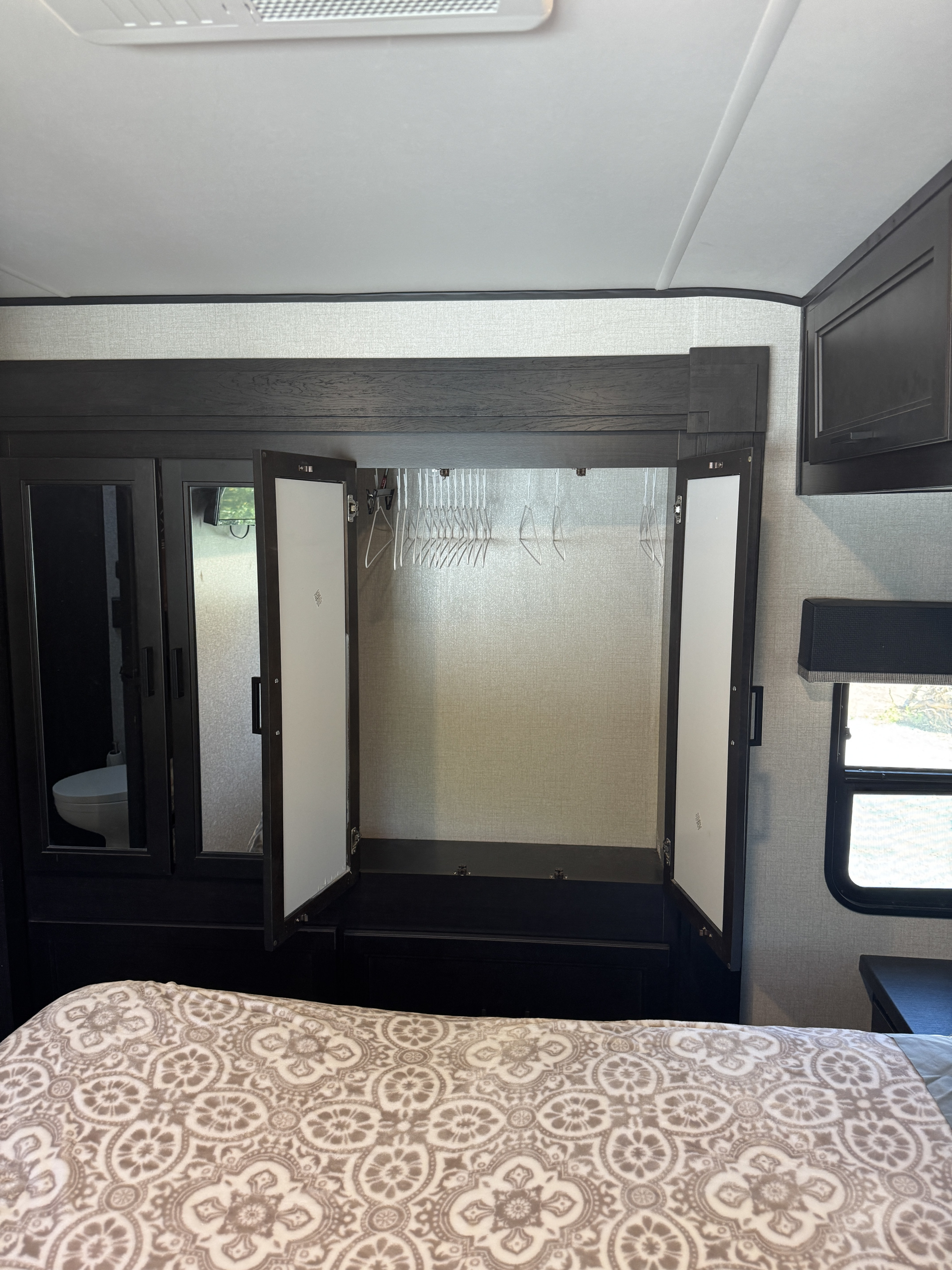 RV rental bedroom: Open wardrobe with hangers, mirrored doors, and comfortable bed with patterned blanket.. Highland Ridge RV Mesa Ridge 2022