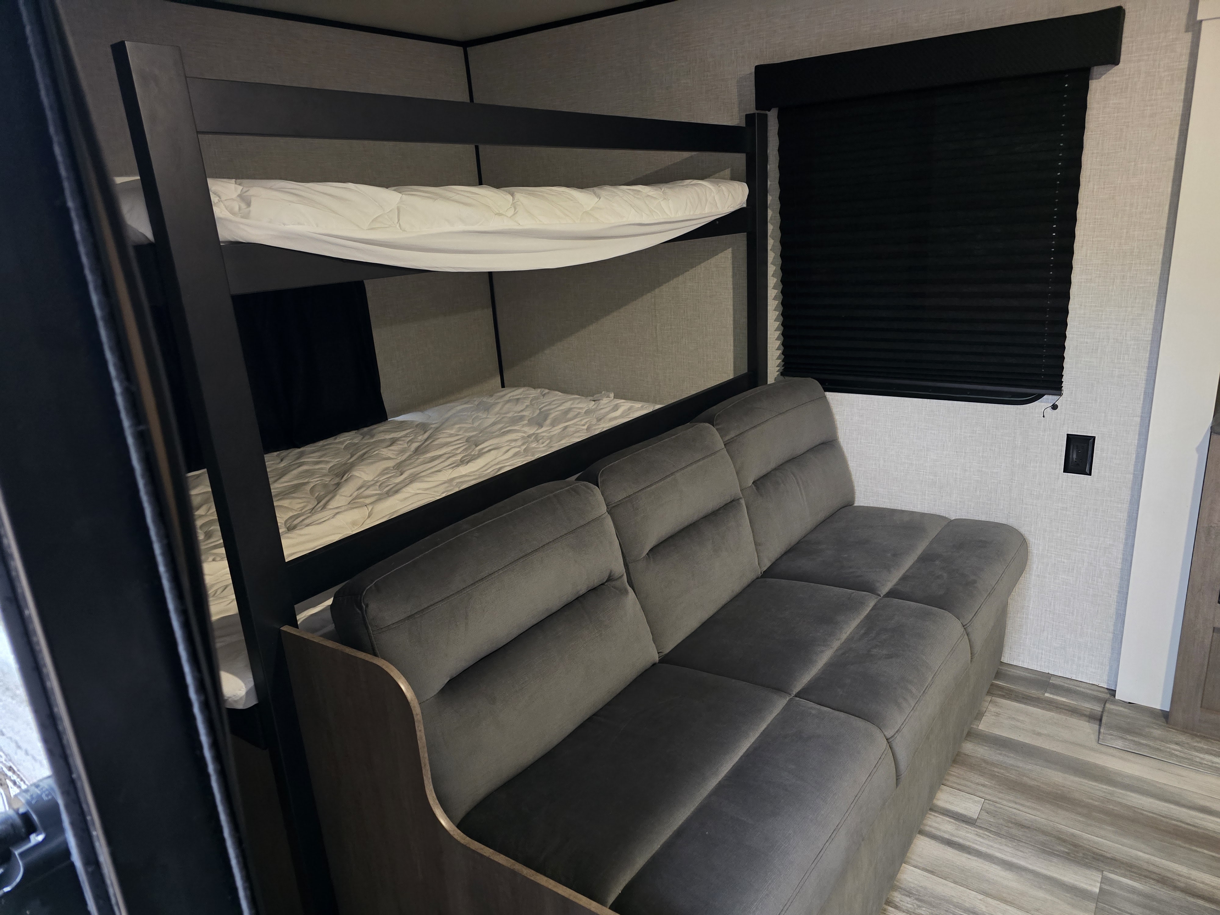 RV rental bedroom and living area: bunk beds with white bedding, a modern grey sofa, and blackout blinds for comfort.. Jayco Jay Flight SLX 2025