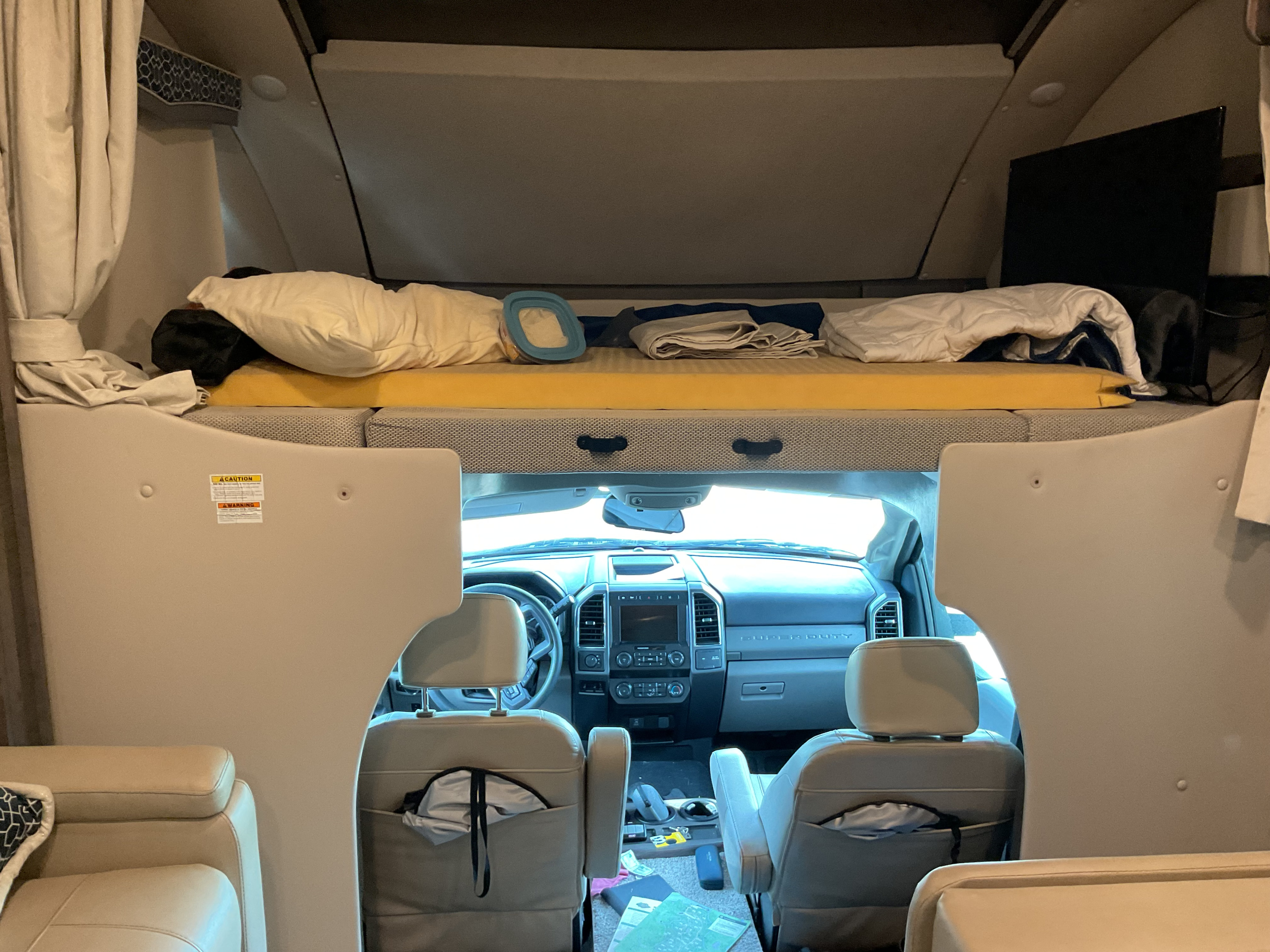 RV rental interior view: over-cab sleeping area with bedding, plus the front cab's dashboard and seats.. Thor Magnitude 2022