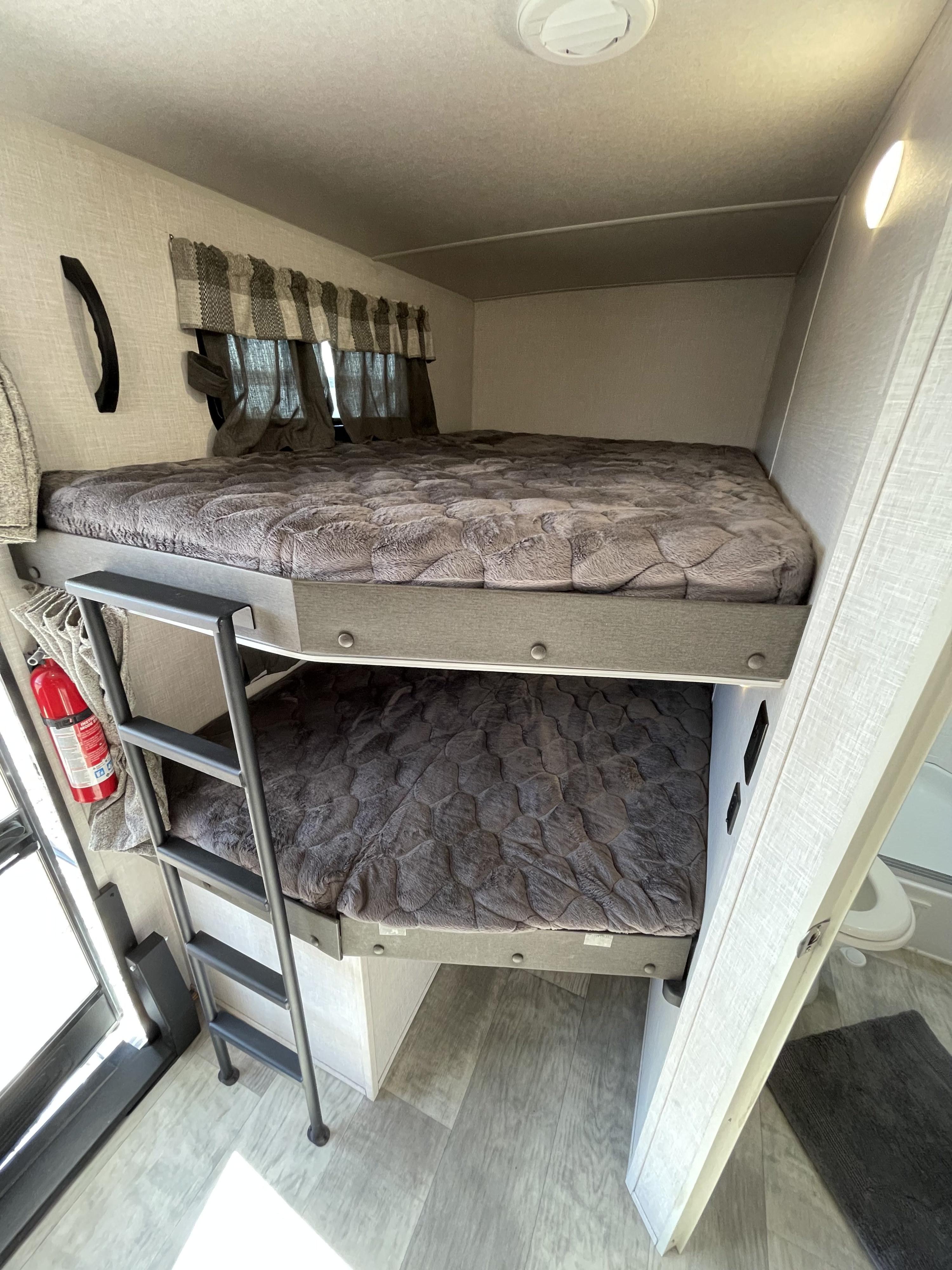 Cozy bunk beds in an RV rental, featuring a ladder, soft grey bedding, and a fire extinguisher for safety.. Forest River Flagstaff Super Lite 2021