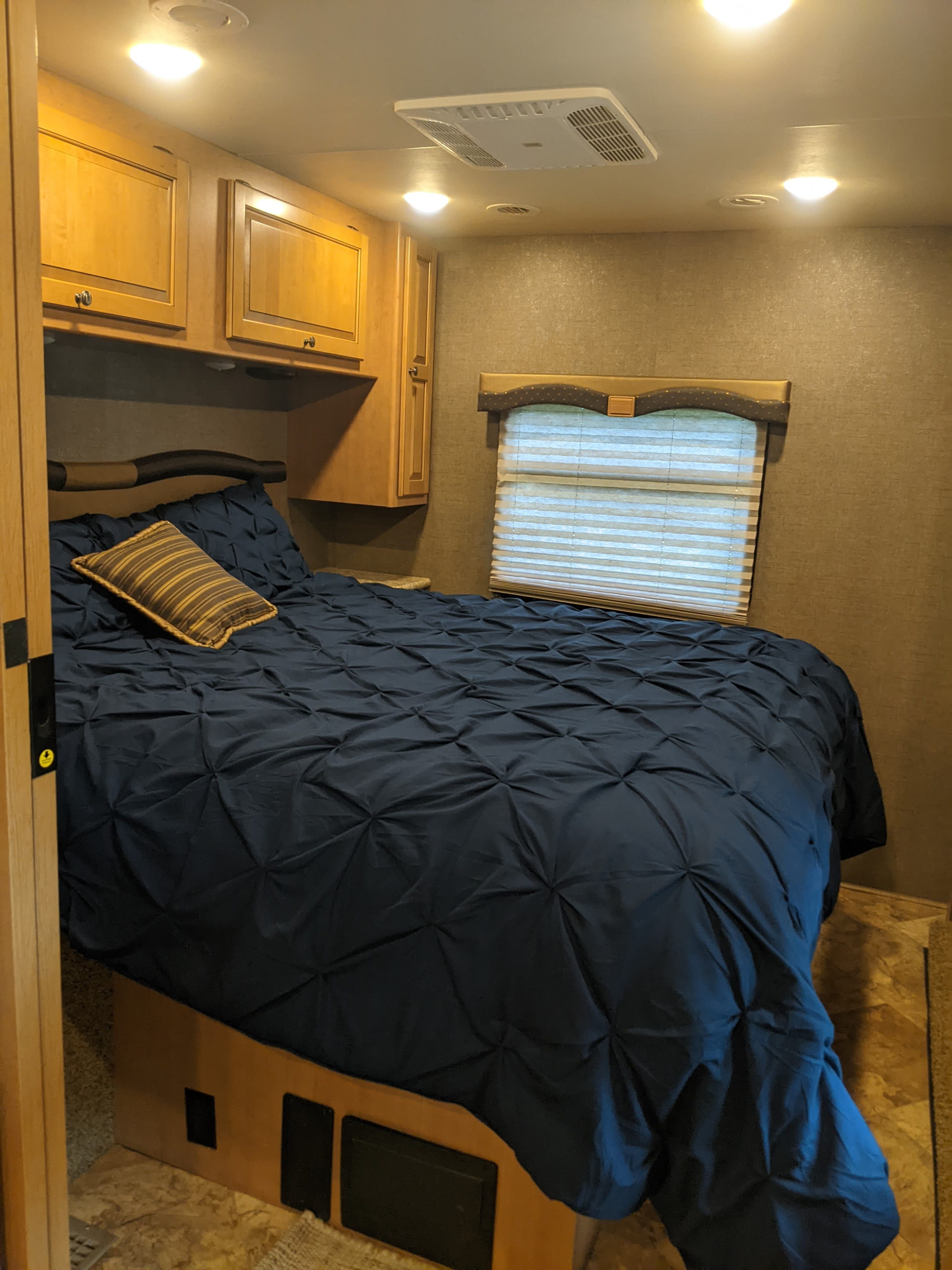 Cozy RV rental bedroom featuring a dark blue comforter, striped pillow, wooden cabinetry, and window blinds, ready for your travels.. Thor Windsport 2017