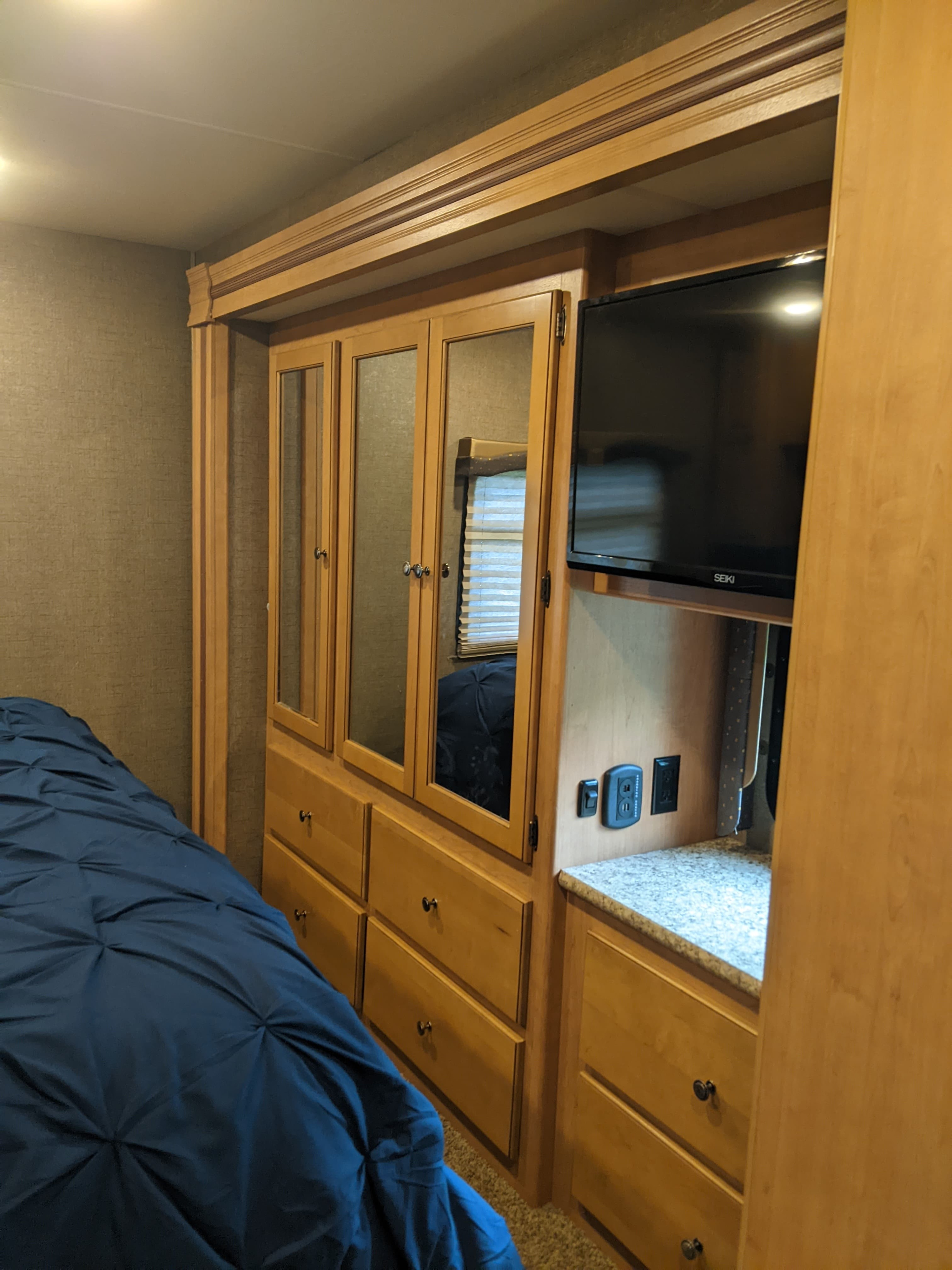 Cozy RV rental bedroom with light wood cabinetry, mirrored wardrobe, blue bed, mounted TV, and charging outlets.. Thor Windsport 2017