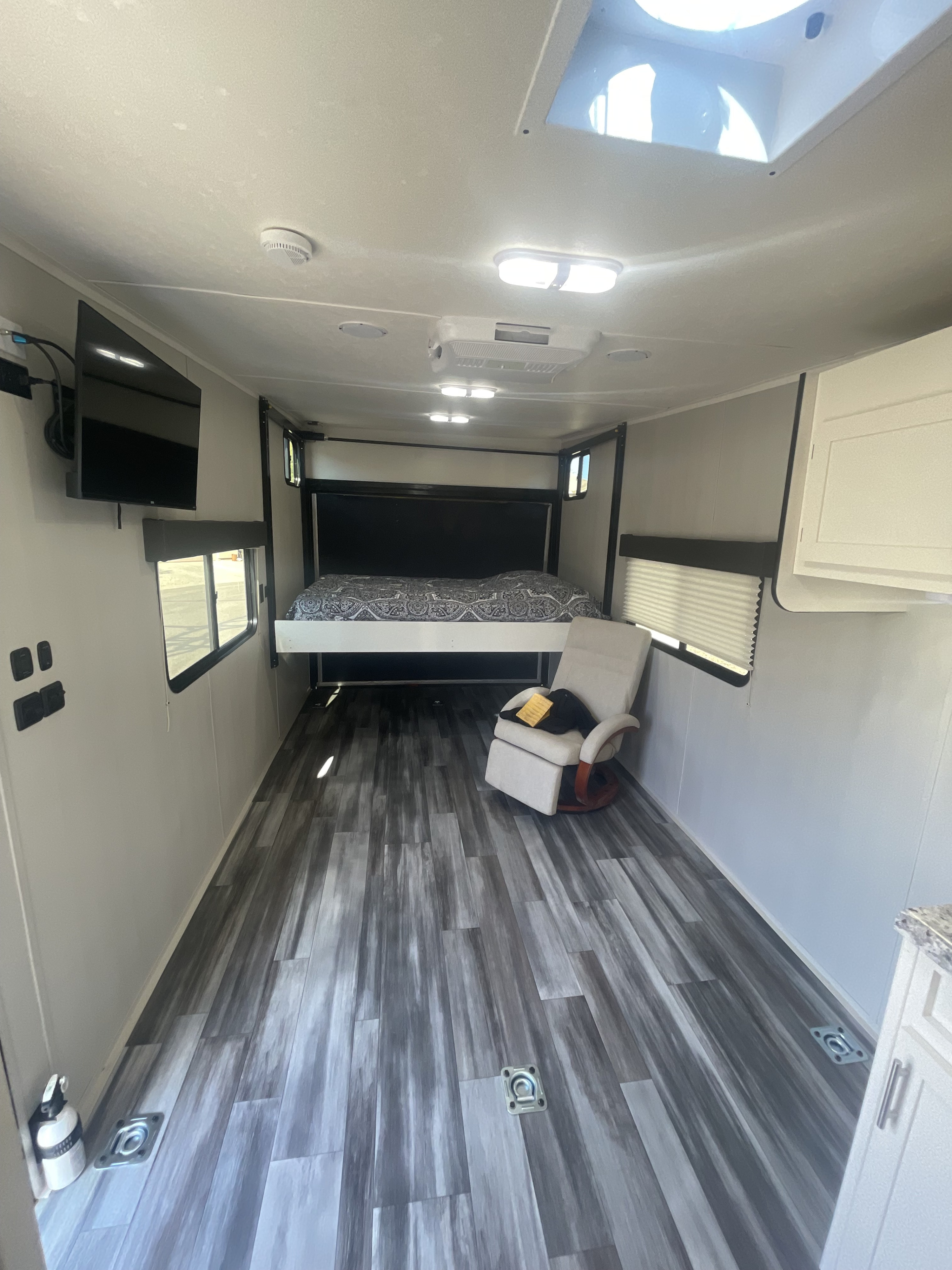 RV rental interior: modern toy hauler living space with elevated bed, comfy recliner, TV, and wood-look laminate floor.. Weekend Warrior 1900fb Toybox 2000