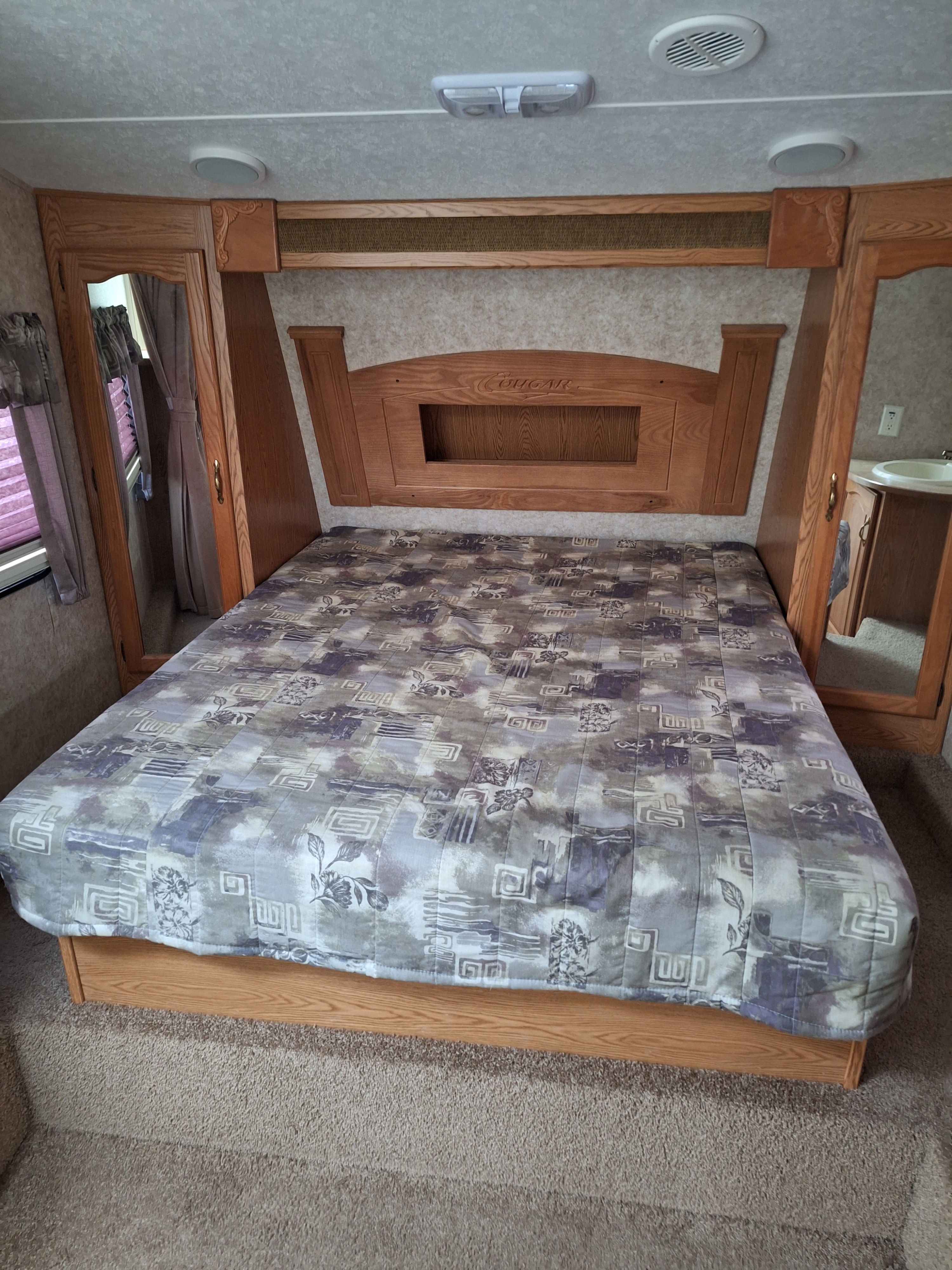 RV rental bedroom with a patterned bedspread, wooden headboard, and built-in cabinets. Features a comfy sleeping area.. Keystone Cougar 278RETS 5th wheel 2007