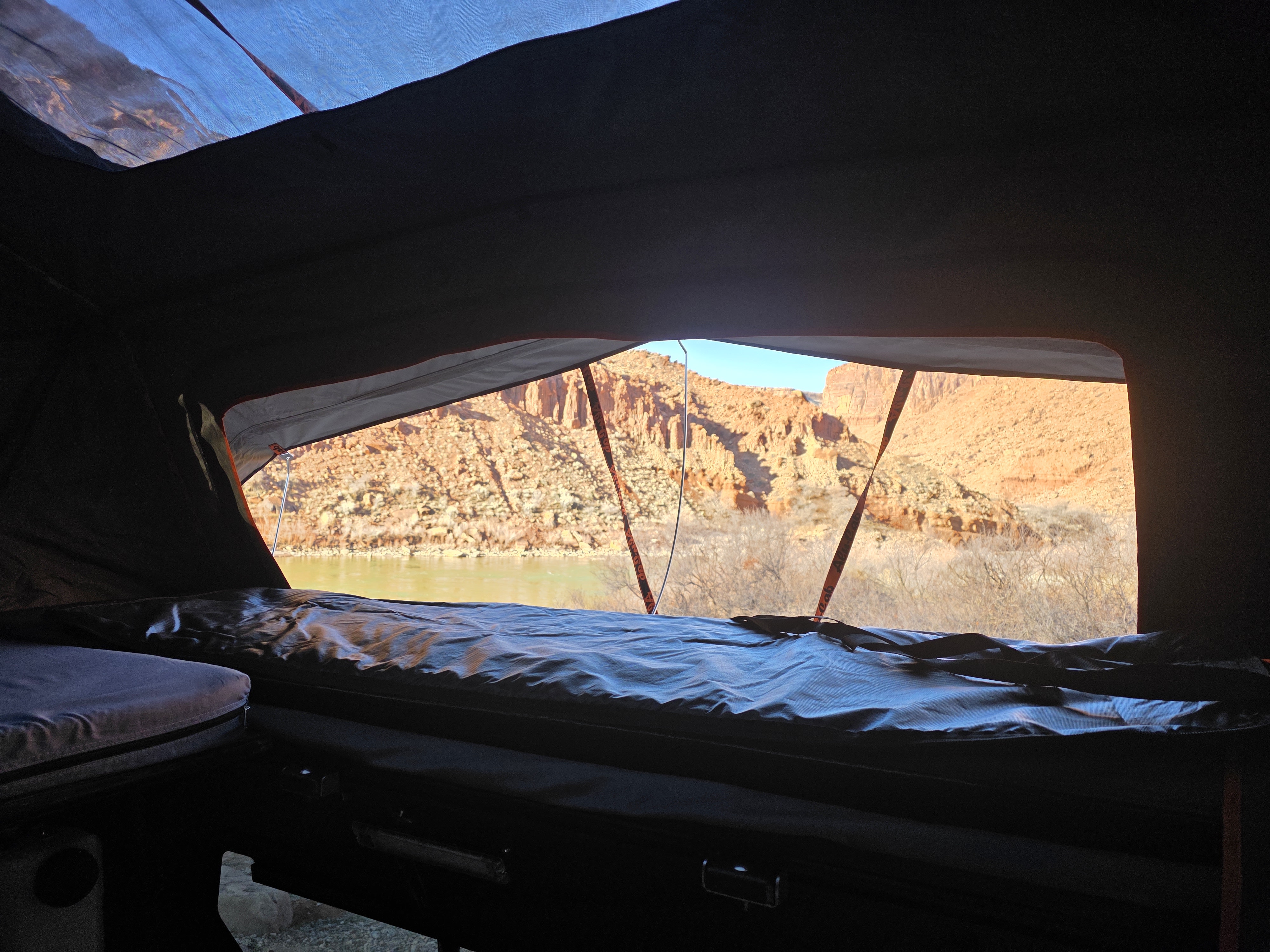 Inside an RV rental, a comfy bed offers stunning views of a river winding through rugged desert mountains. Ideal for outdoor adventures.. Toyota Tundra 2019
