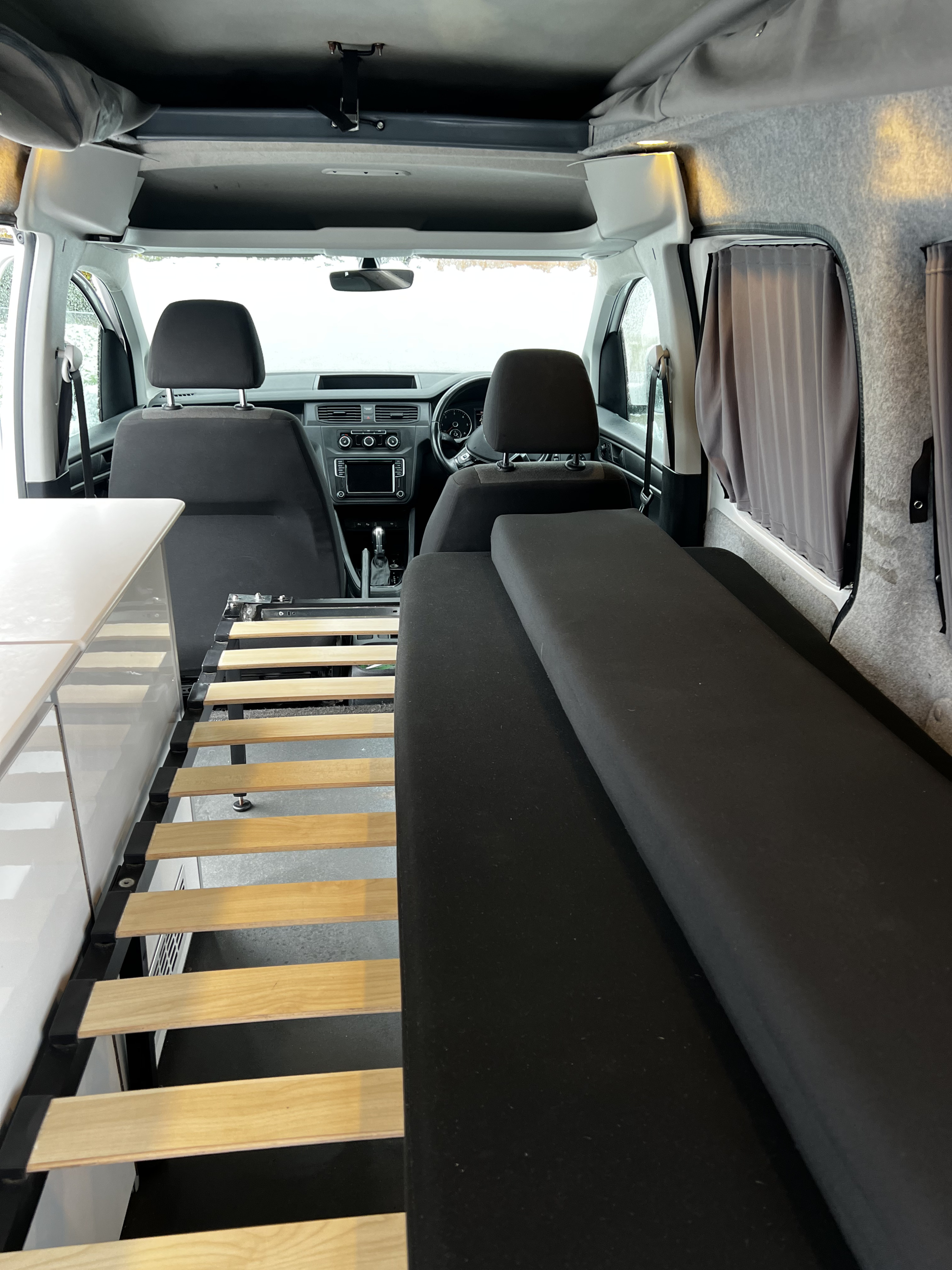 Cozy RV rental interior with a slatted bed base, comfortable cushions, front cab view, and pop-top roof.. Volkswagen Caddy Maxi 2020