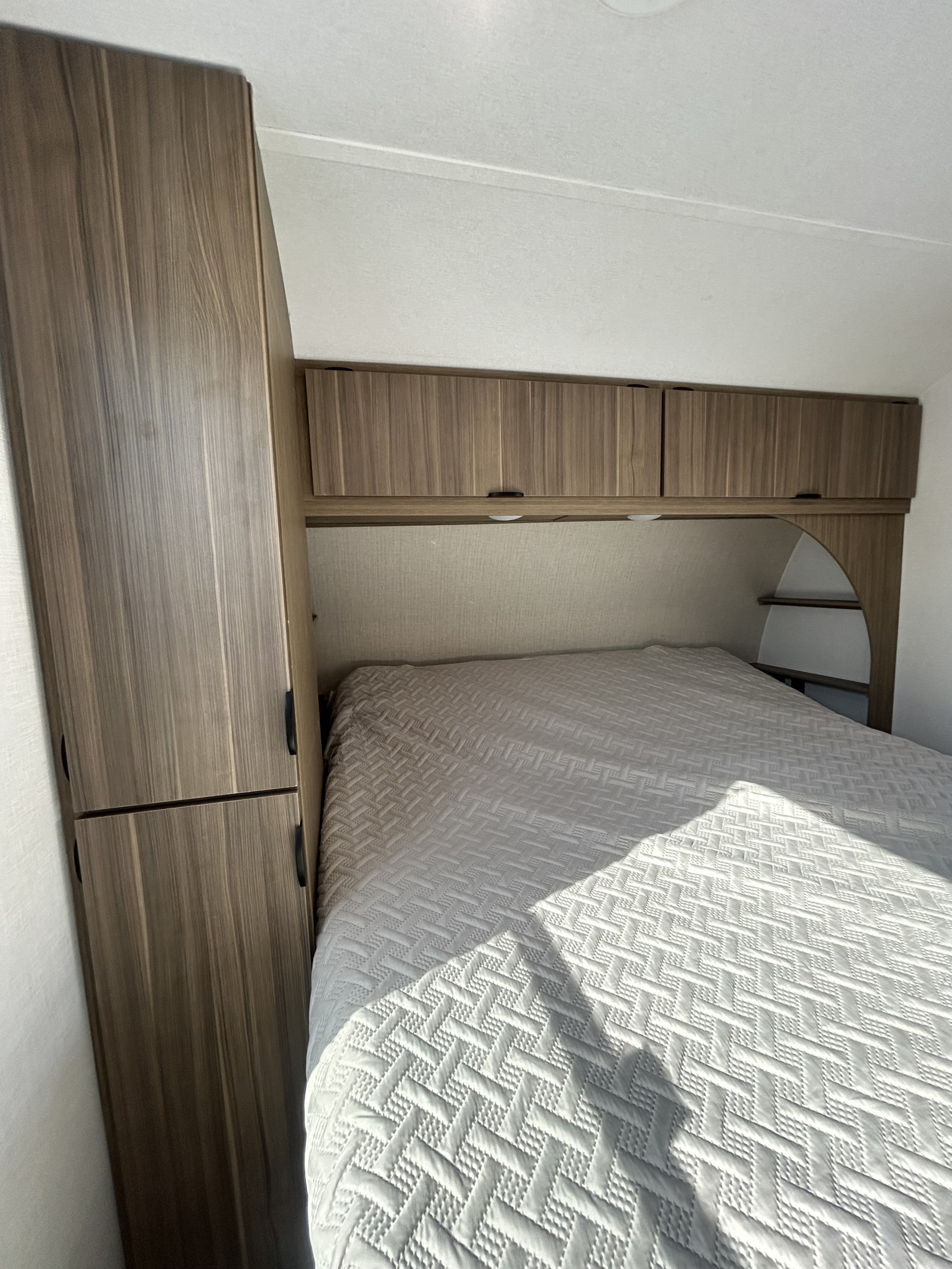 Cozy RV rental bedroom with a comfy bed, wood-grain wardrobe, and overhead cabinets.. Forest River Salem 2025