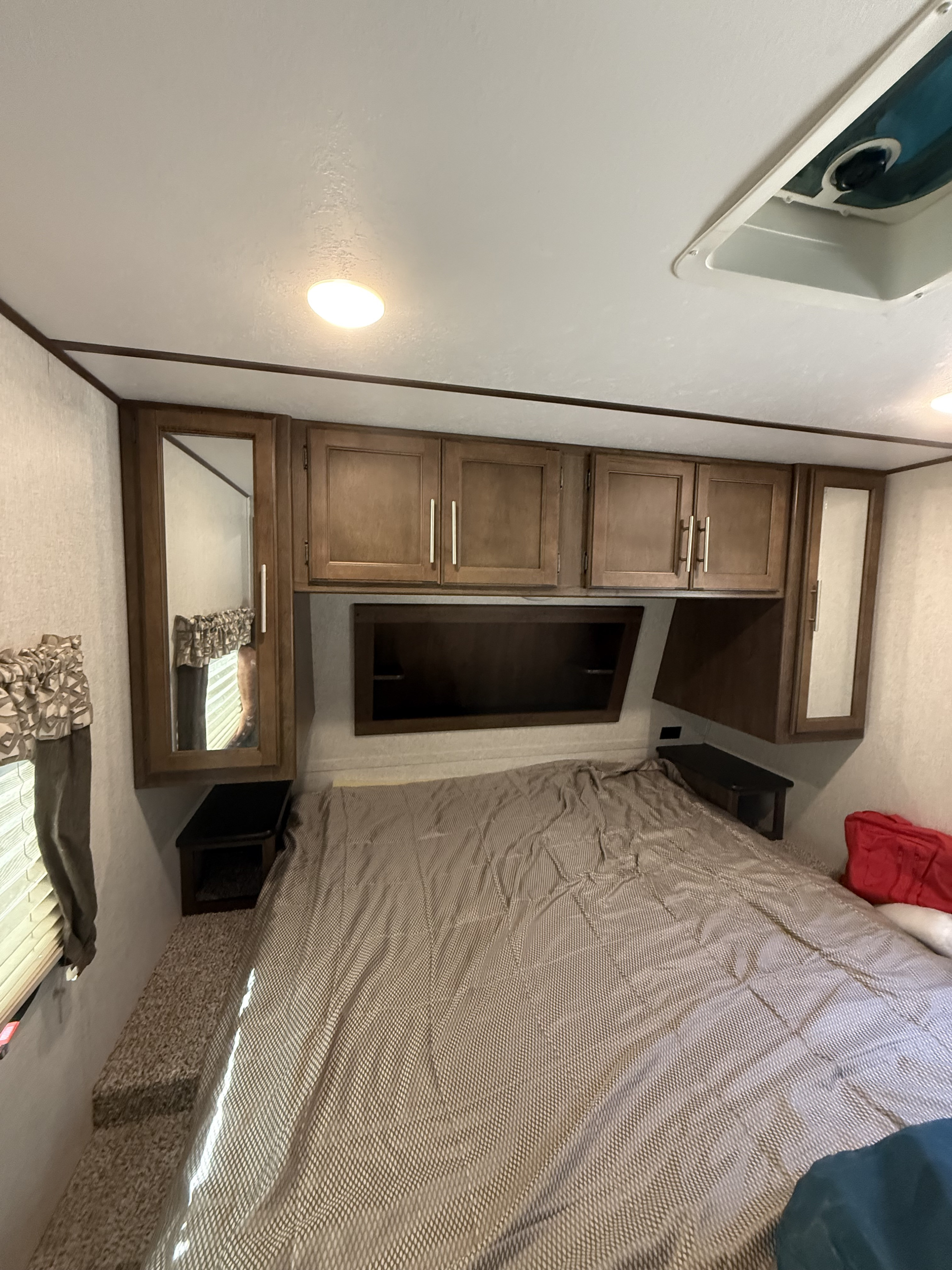 Cozy RV rental bedroom with overhead storage, mirrored cabinets, recessed shelf, and patterned comforter on a bed.. Keystone RV Cougar 2018