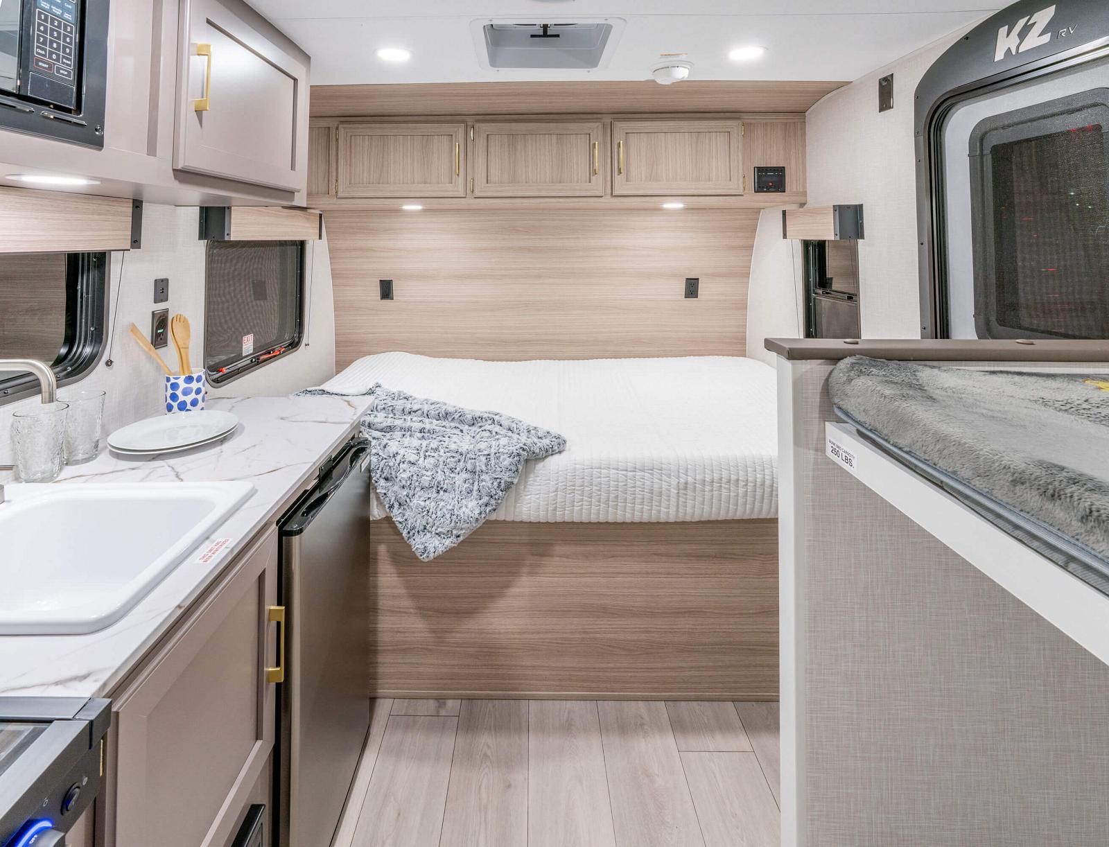 This RV rental interior features a bed, kitchenette with sink, microwave, fridge, and ample overhead storage.. KZ Sportsmen Classic 130BH 2026