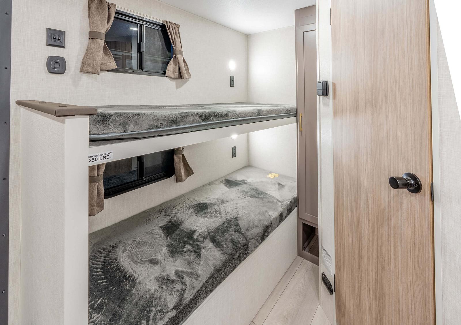 Inside this RV rental, a compact bunk bed room features two cozy beds with windows, curtains, lights, and outlets.. KZ Sportsmen Classic 130BH 2026