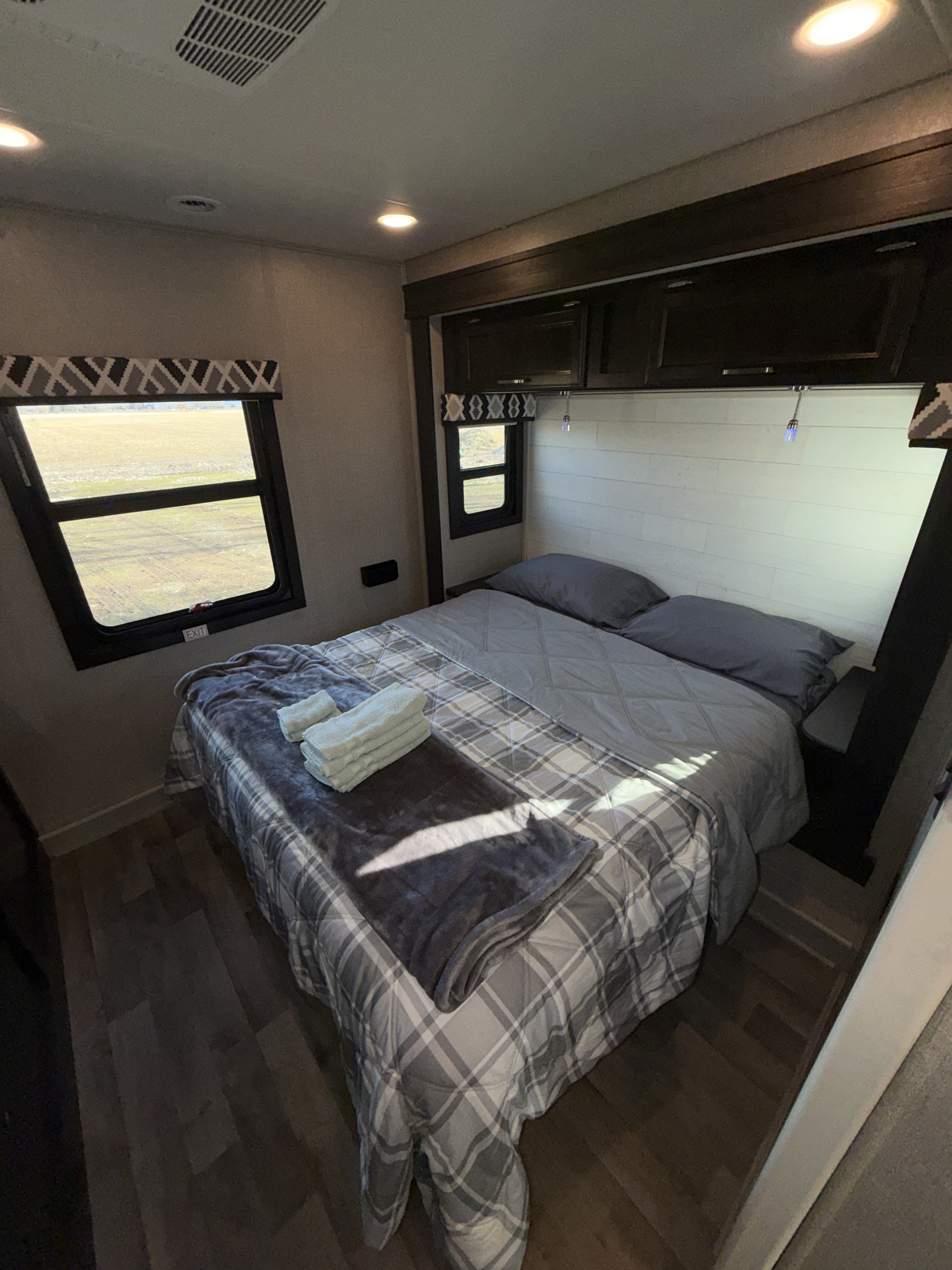 Cozy RV rental bedroom with plaid bedding, overhead storage, and a scenic window view, perfect for your next adventure.. Jayco Greyhawk 2021