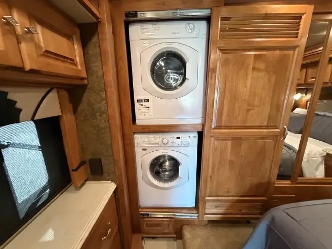 Interior of an RV rental showing a stacked washer and dryer unit for laundry convenience, surrounded by wood cabinetry.. Tiffin Phaeton 36 QHS 2015