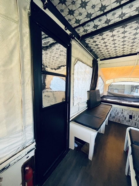 This rv rental features a pop-up camper interior with a starry ceiling, built-in benches, and sleeping area.. Coleman Grand Tour Laramie 1989