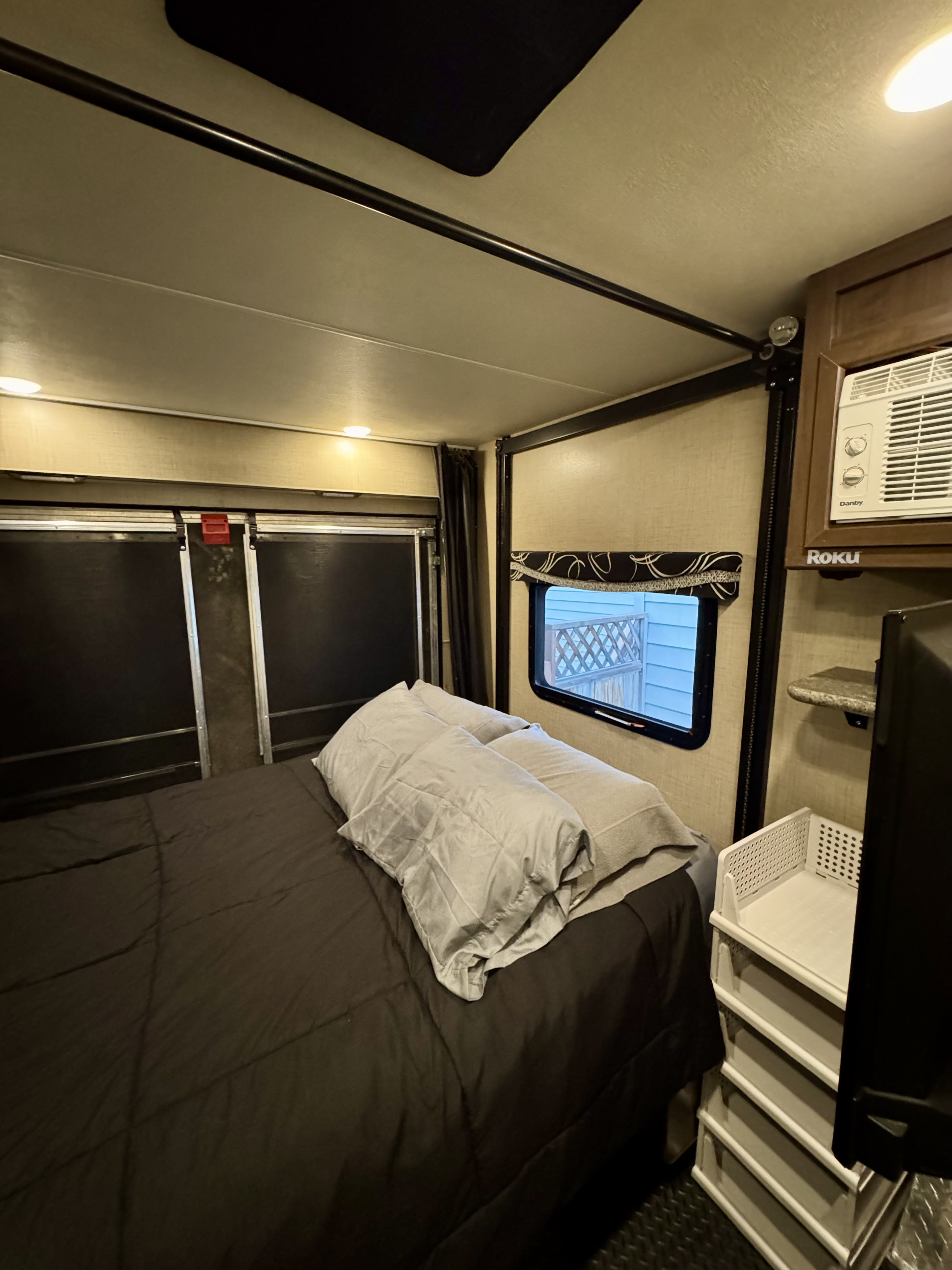 RV rental bedroom featuring a full bed, window view, AC, and convenient tiered storage unit.. Thor Outlaw 2019