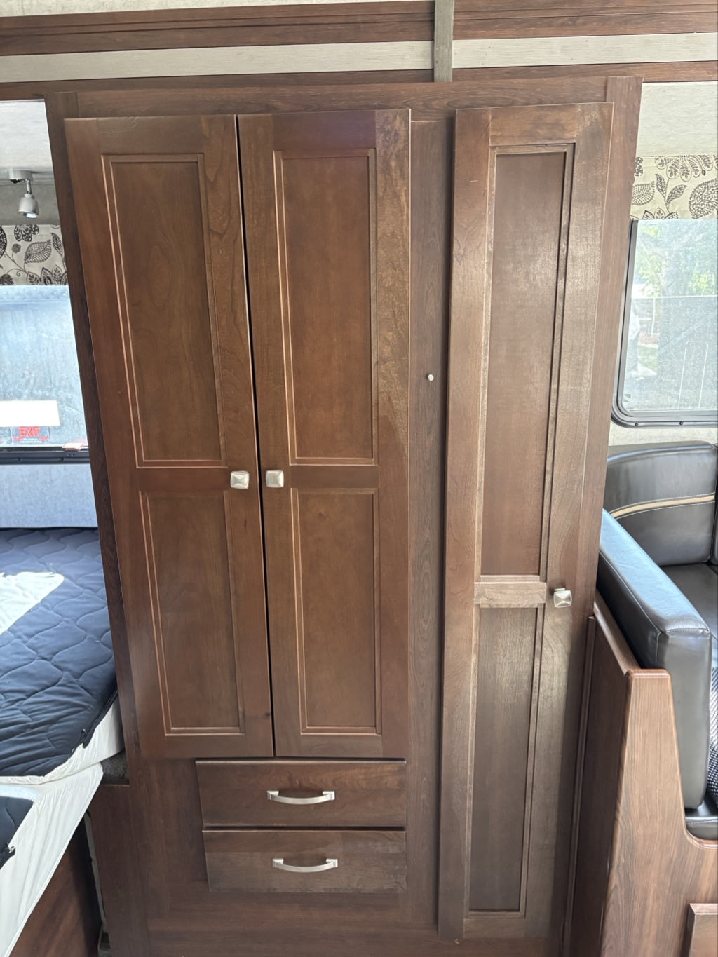 View of a dark wood wardrobe with two doors & two drawers, integrated into an RV rental interior next to a bed & seating.. Forester MBS 2018