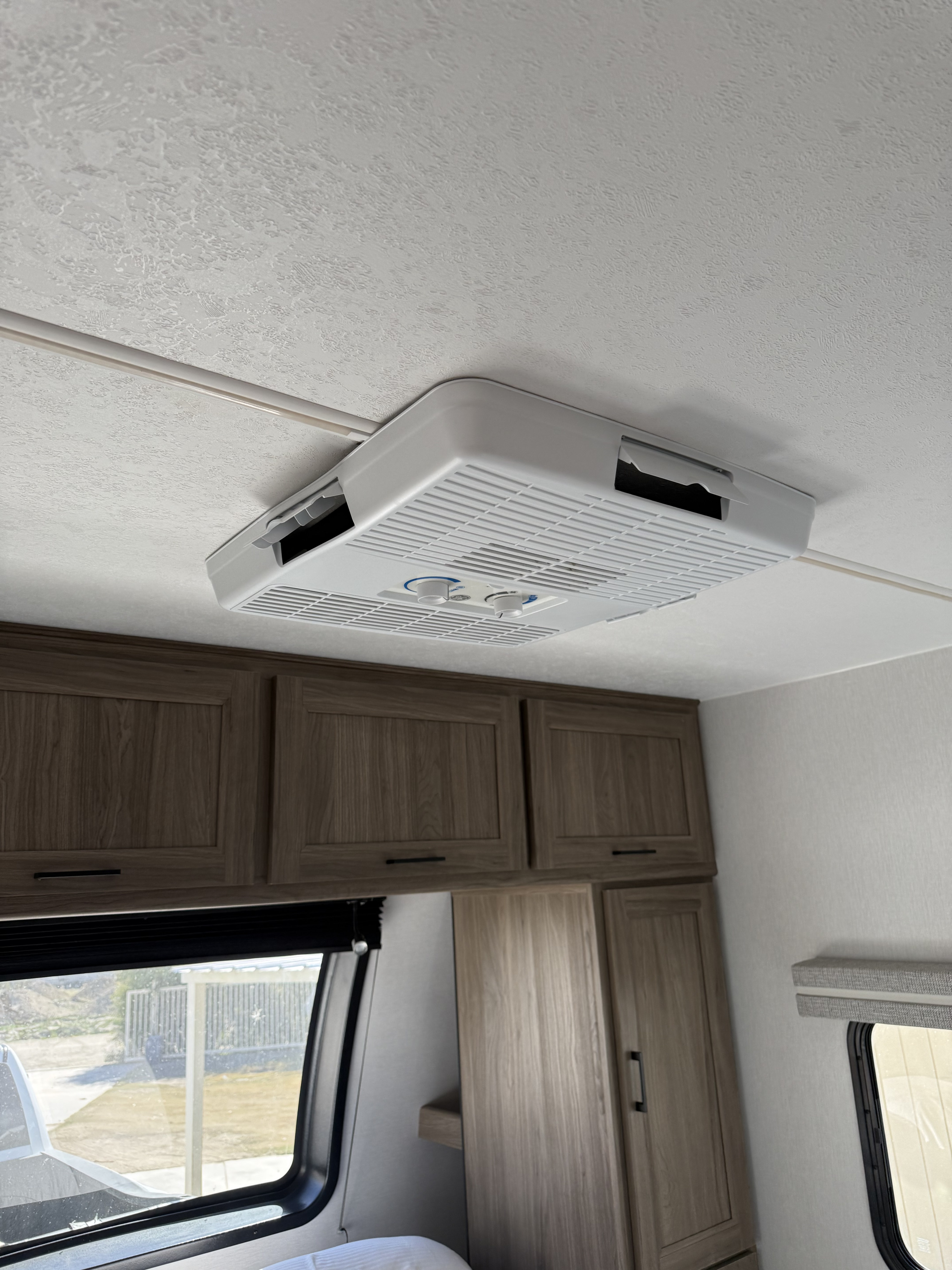 RV rental interior showing a ceiling-mounted AC unit, light wood overhead cabinets, and a window in a modern travel trailer.. Forest River Coachmen Freedom Express 2025