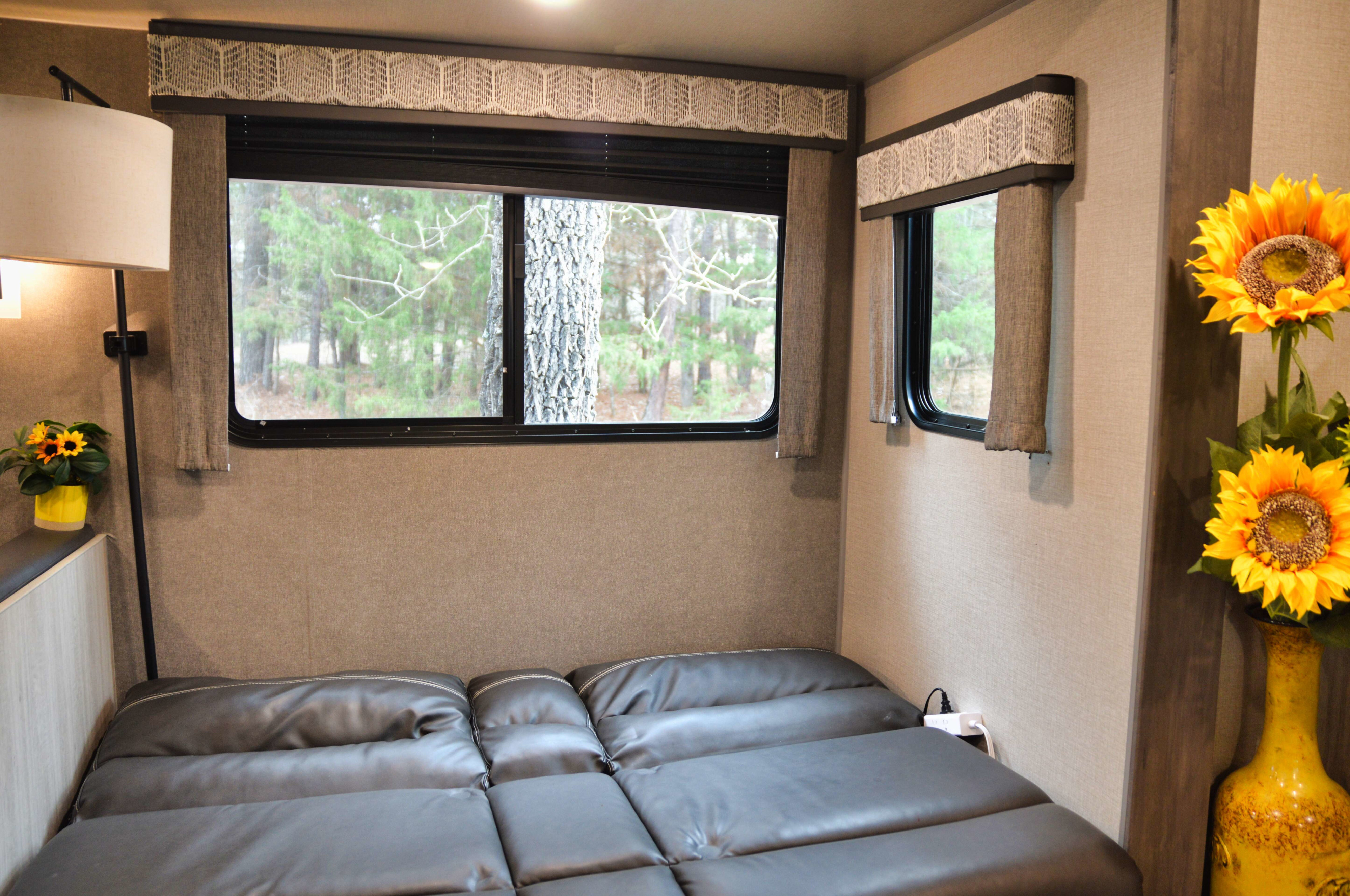 Enjoy nature from this cozy RV rental bedroom. Features a comfy bed, forest views, and vibrant sunflower decor.. Coachmen Catalina 2022