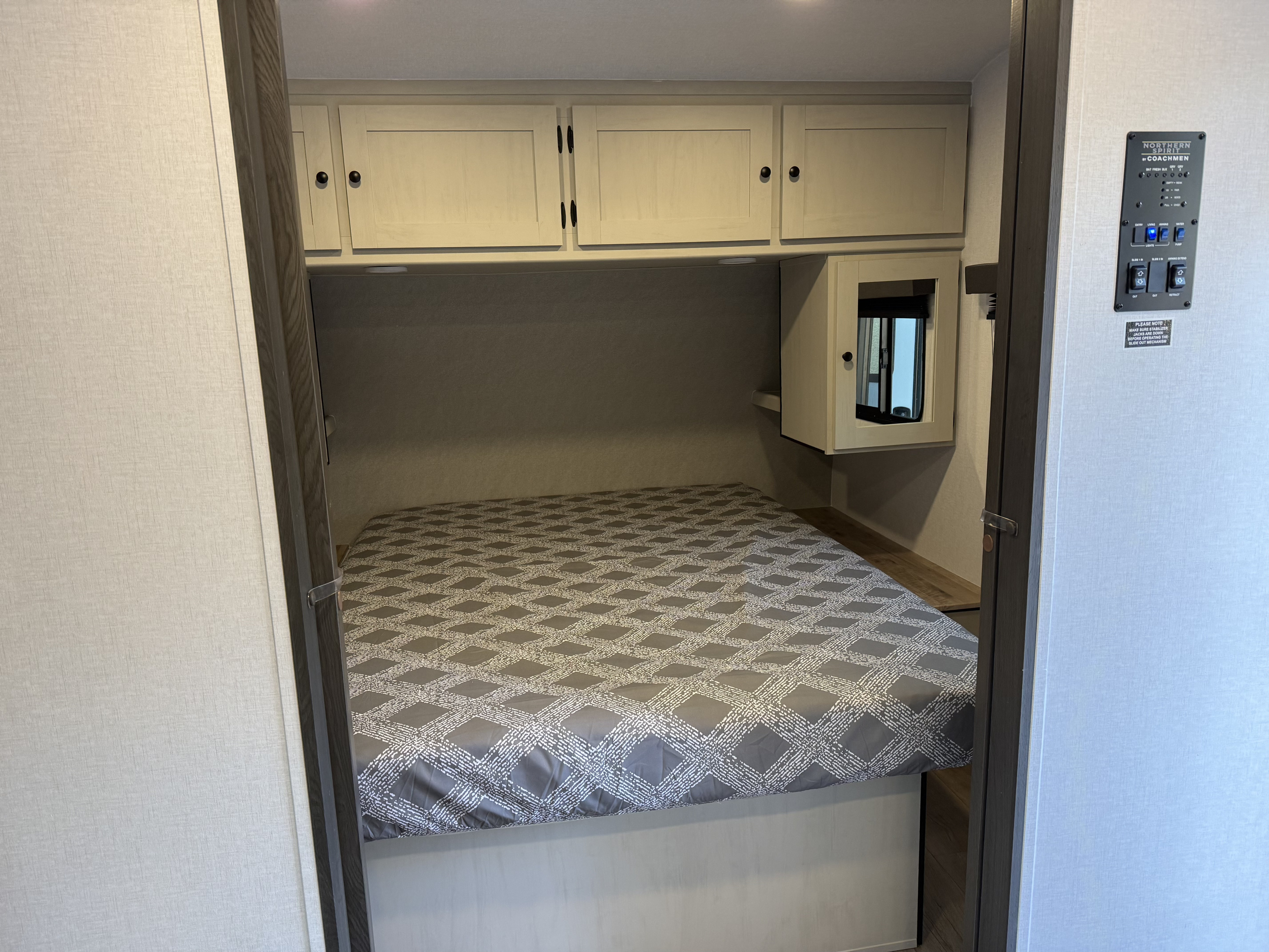 RV rental bedroom with light wood cabinets, a patterned bed, and a Northern Spirit control panel for an efficient living space.. Coachmen Spirit 29BH 2026