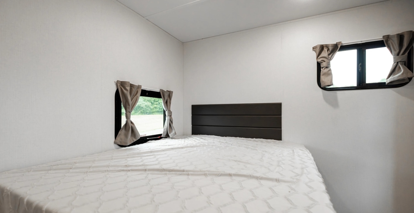 Spacious RV rental bedroom with a large bed, modern dark headboard, and two windows with tie-back curtains. Clean white walls.. Forest River Shasta I-5 2025