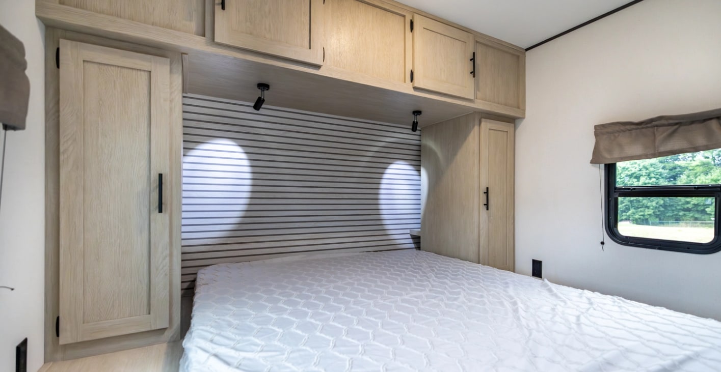 Comfortable RV rental bedroom with a white bed, overhead cabinets, bedside wardrobes, and a window for scenic views.. Forest River Shasta I-5 2025