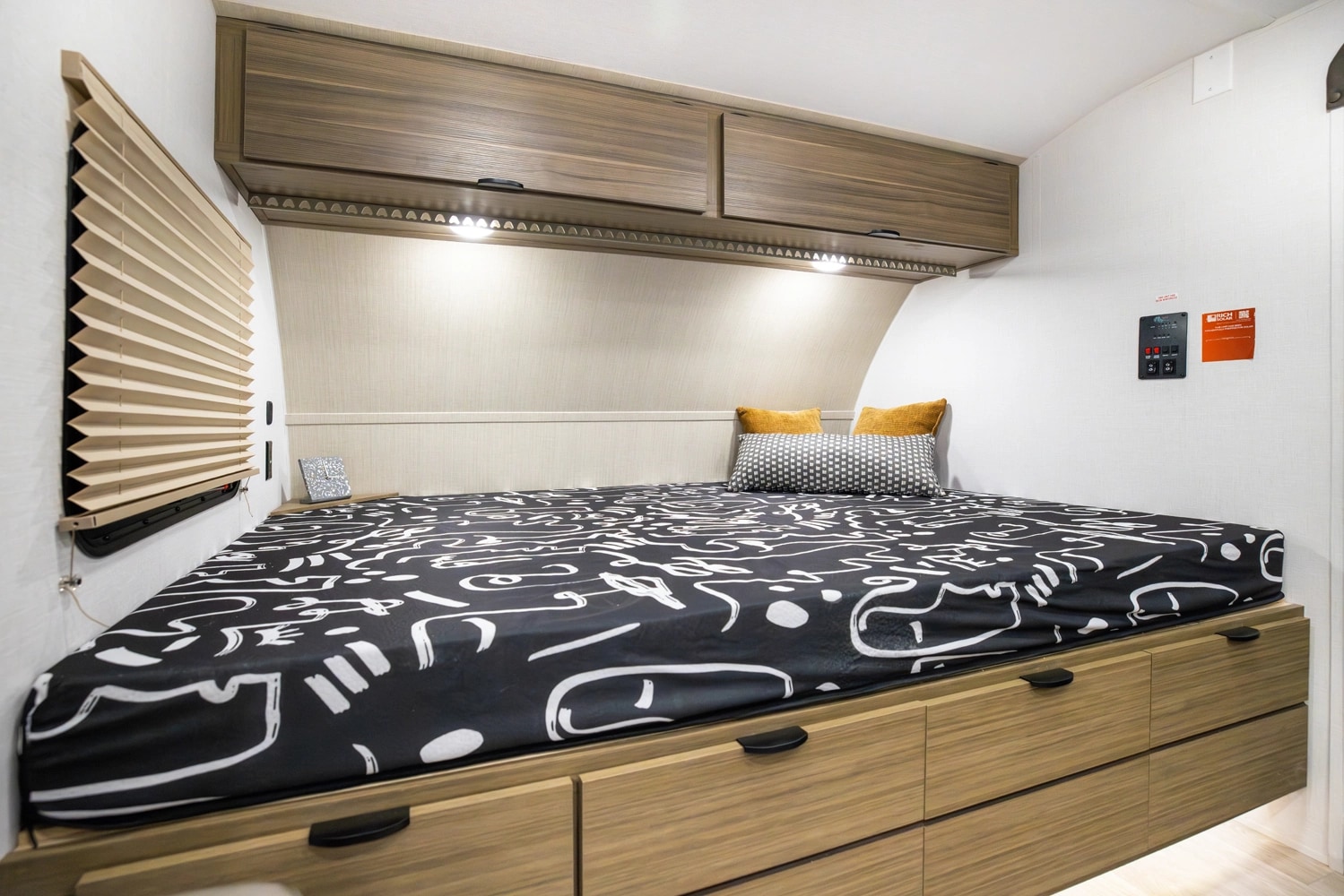 This modern RV rental bedroom offers a comfortable bed, ample storage, and convenient wall controls for a cozy travel experience.. Forest River Wildwood 178 ICE 2026