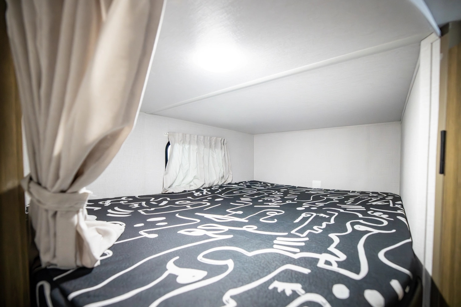 RV rental bunk bed featuring an abstract patterned sheet, white walls, and privacy curtain for a cozy sleep space.. Forest River Wildwood 178 ICE 2026