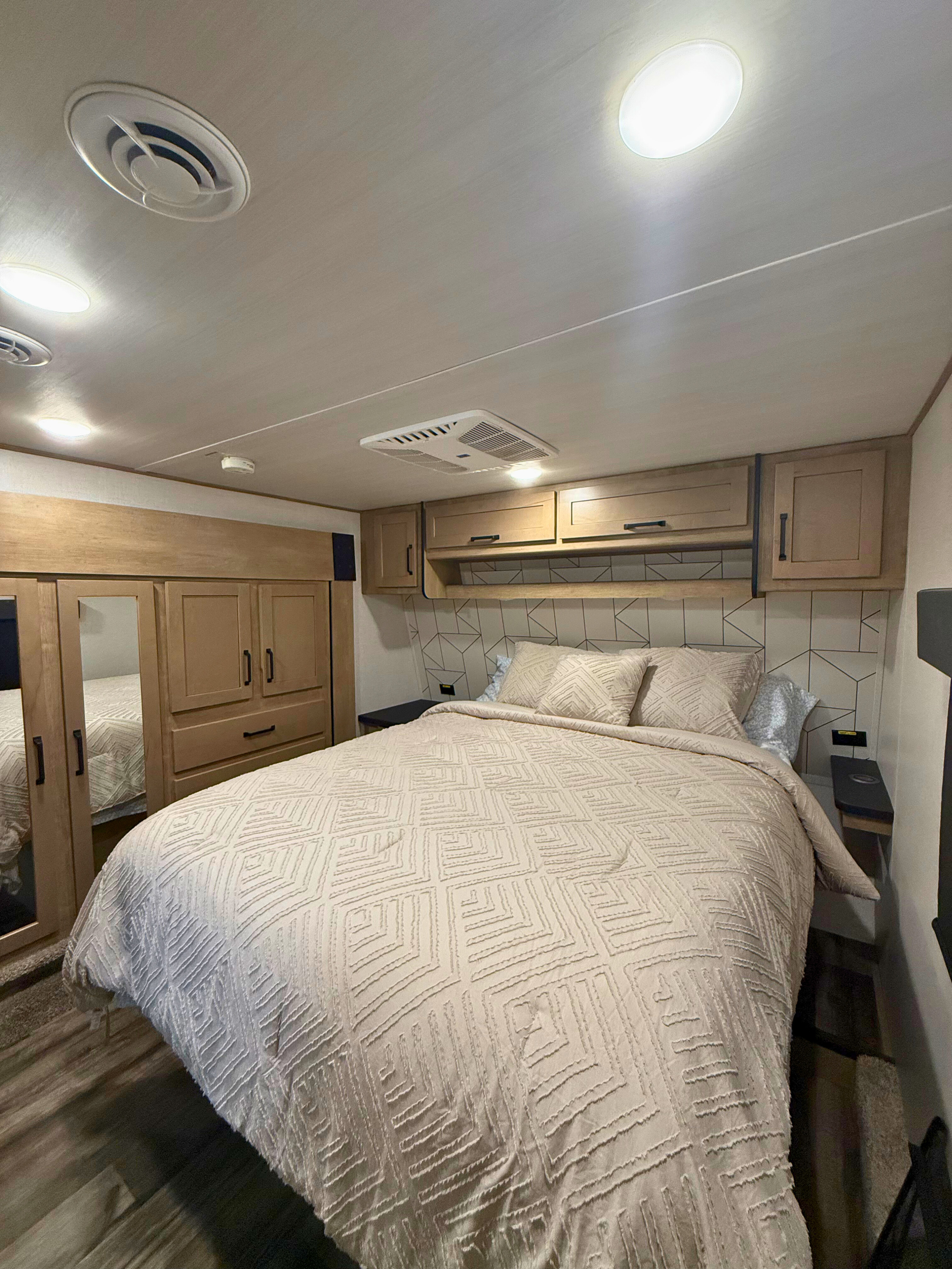 Discover comfort in this RV rental bedroom: a large bed with light, textured covers, ample overhead cabinets, and a stylish geometric headboard.. Keystone RV Raptor Toy Hauler 2022