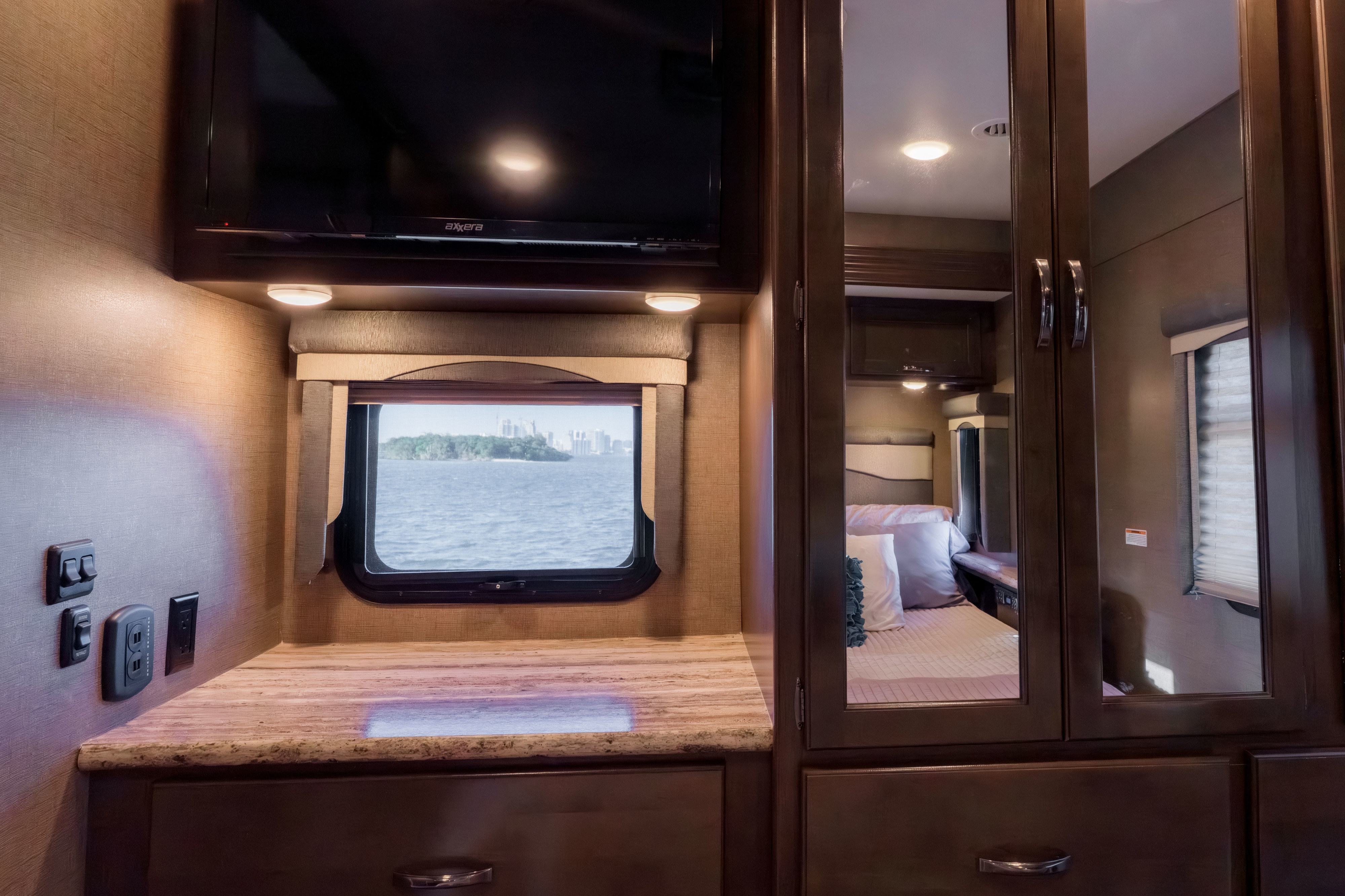 This RV rental offers a compact, functional space with a TV, counter, and scenic water view. Mirrored closet door reflects the cozy bedroom.. Thor A.C.E. 2018