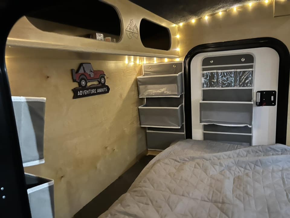 Explore a cozy RV rental: comfy bed, string lights, and clever storage solutions for your next adventure.. Outbound Trailer Outbound Extreme 2026