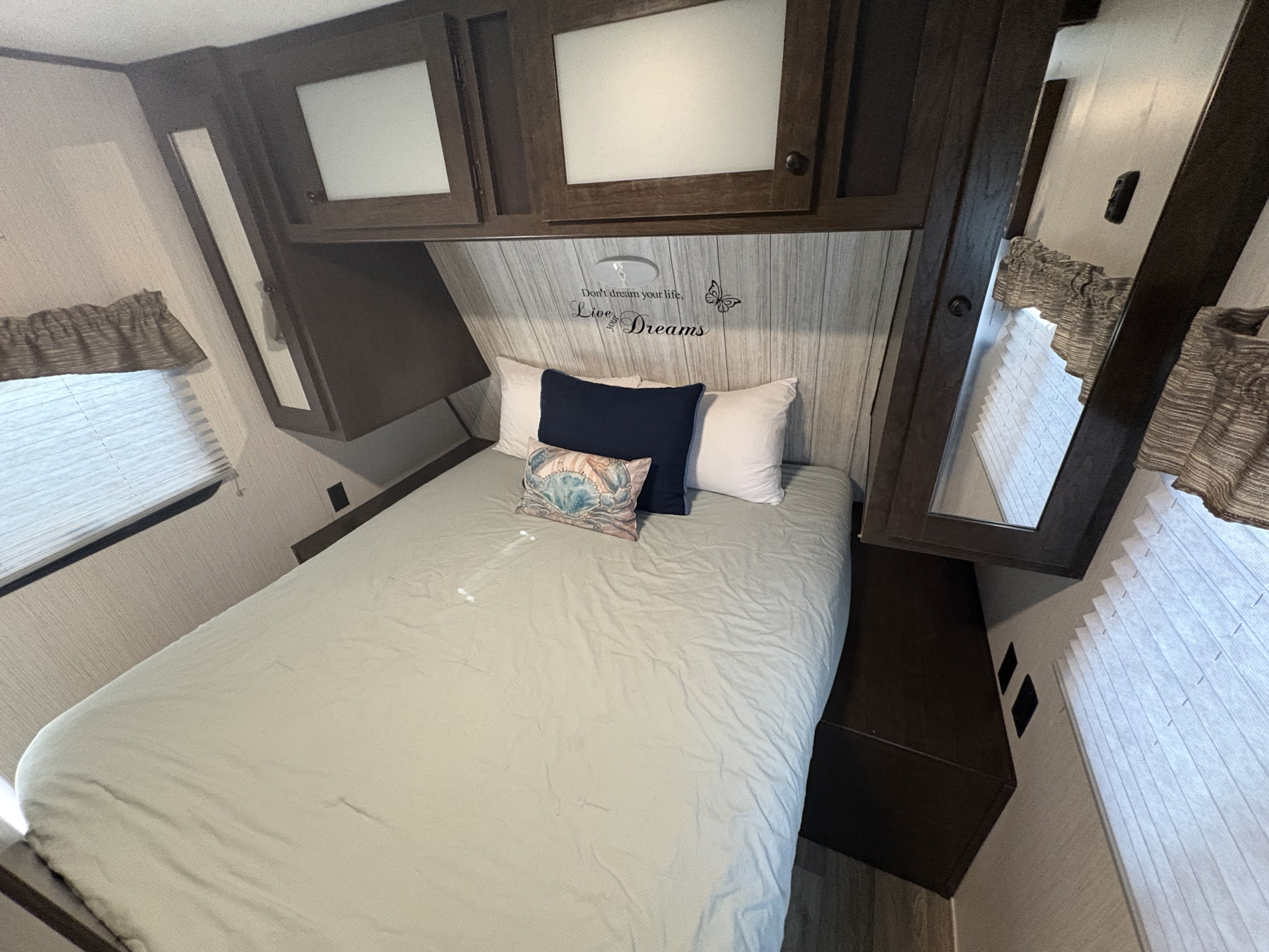 Cozy rv rental bedroom featuring a bed, overhead cabinets, and windows with blinds.. Heartland RVs Pioneer 2021