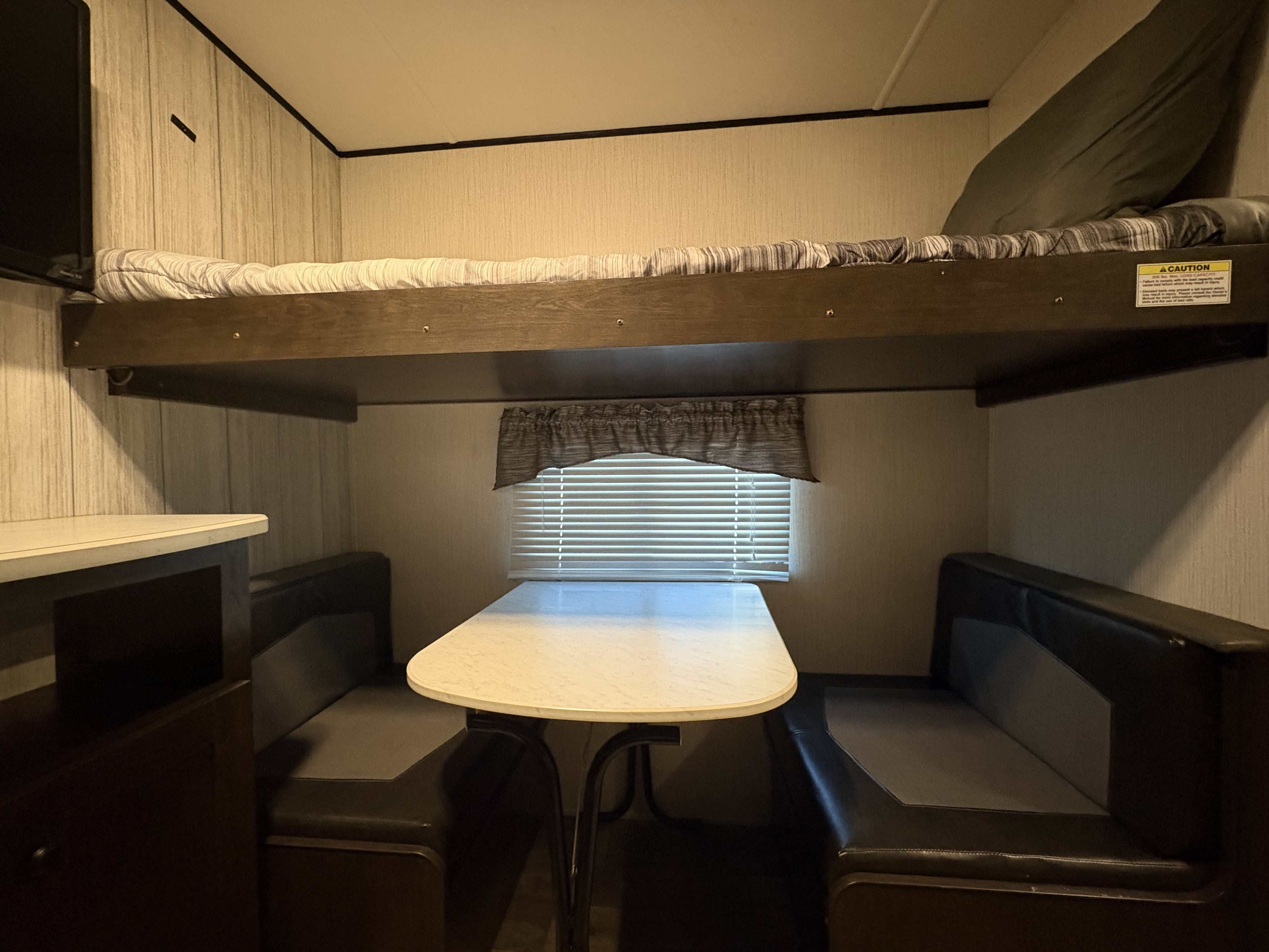 Inside an RV rental: a bunk bed positioned above a cozy dinette area with a table and bench seating. Ideal for compact family adventures.. Heartland RVs Pioneer 2021