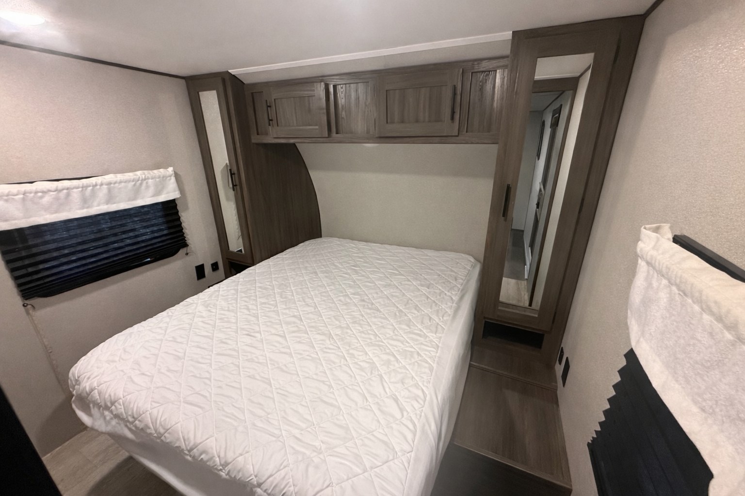 Cozy RV rental bedroom featuring a queen bed with white bedding, overhead cabinets, and mirrored wardrobes for storage.. Forest River Shasta 2021
