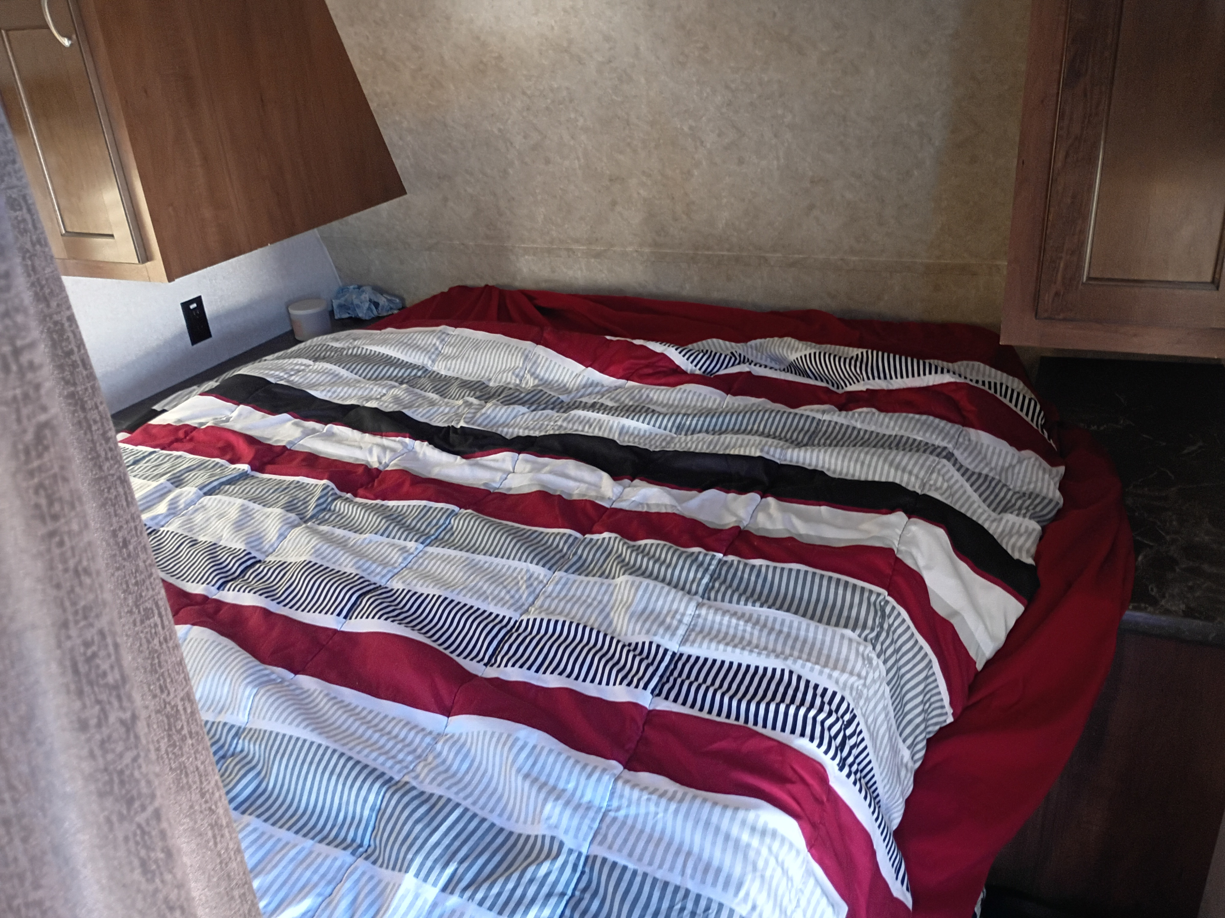 Cozy RV rental bedroom featuring a bold red, white, black, & grey striped comforter & wood cabinets.. Jayco Jay Flight SLX 2017