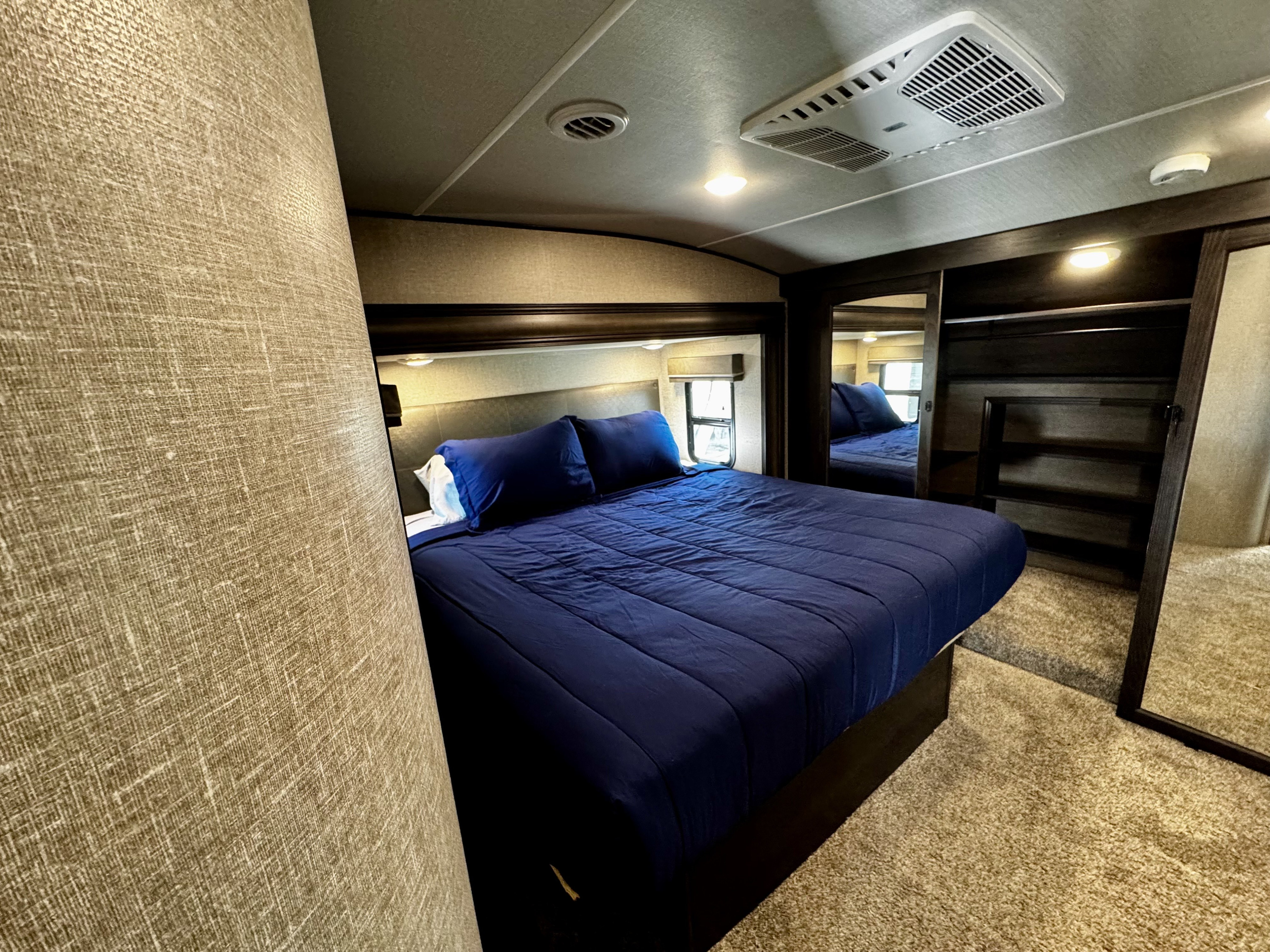 Cozy RV rental bedroom with a dark blue bed, windows, and mirrored wardrobe for comfortable travel.. Grand Design Reflection 2022