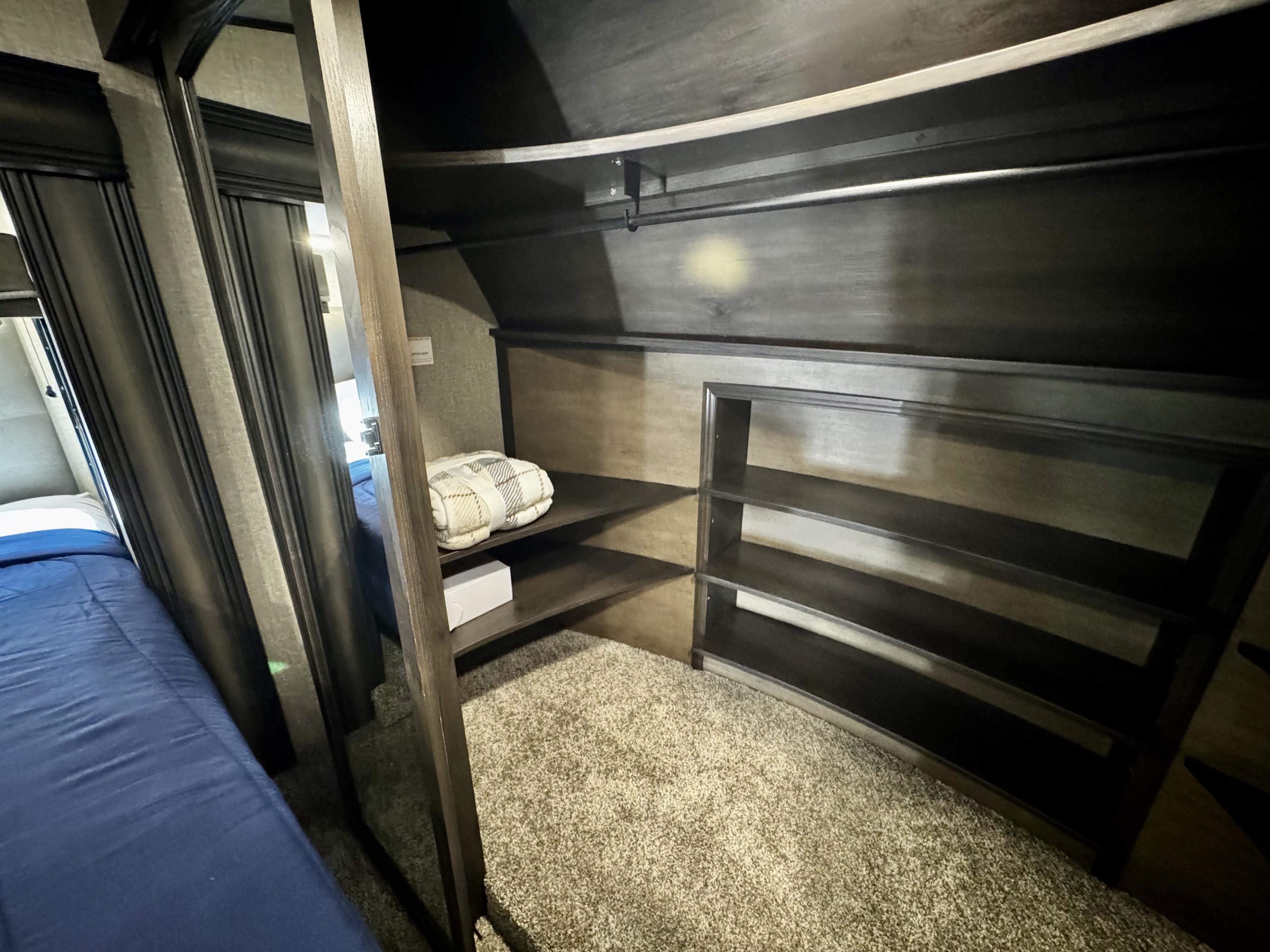 Inside an RV rental: dark wardrobe with shelving, hanging rod & cozy blue bed in the compact bedroom.. Grand Design Reflection 2022