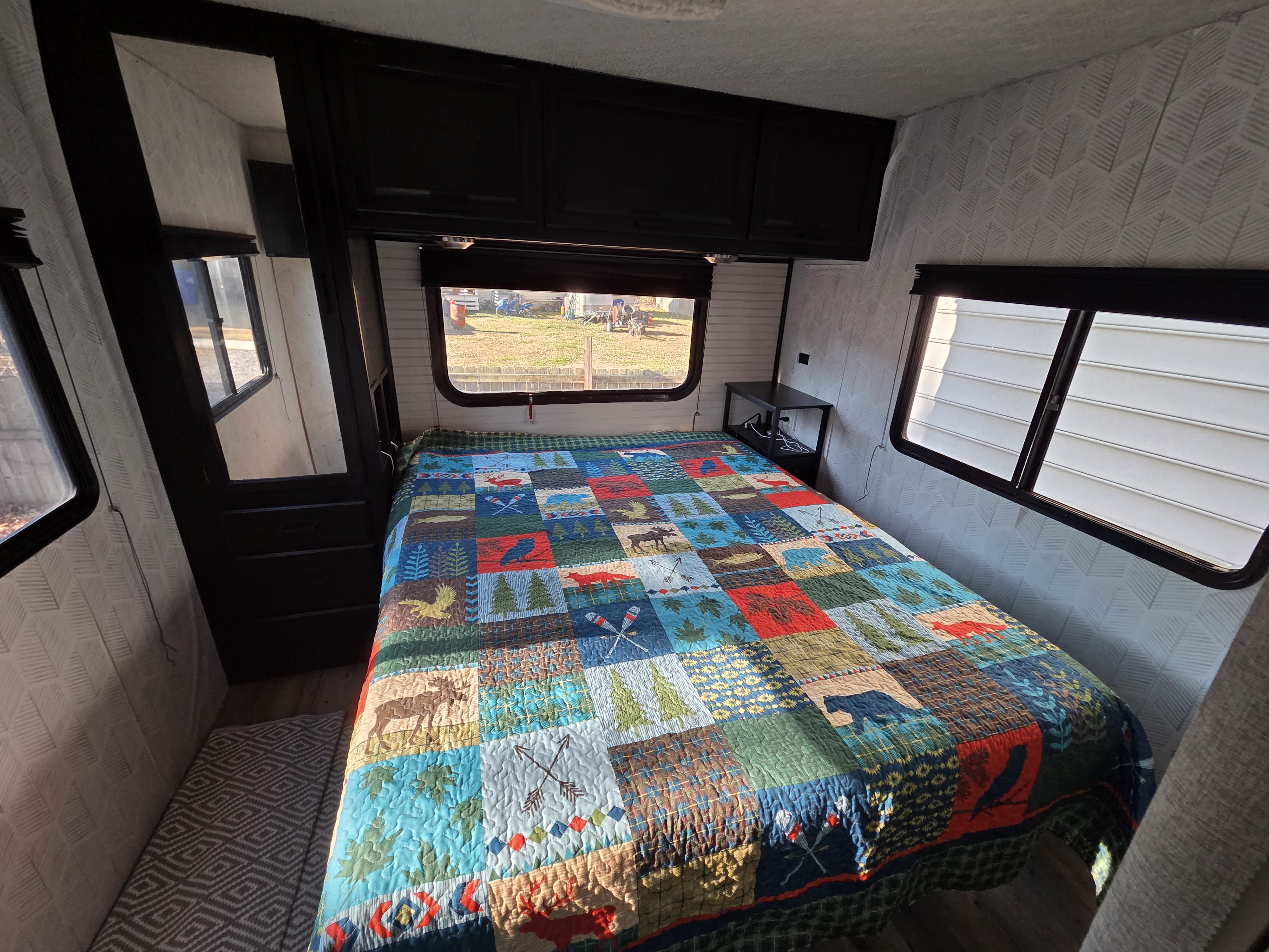 Cozy RV rental bedroom with a nature-themed quilt, overhead cabinets, and windows offering an outdoor view.. Winnebago Minnie Winnie 2002