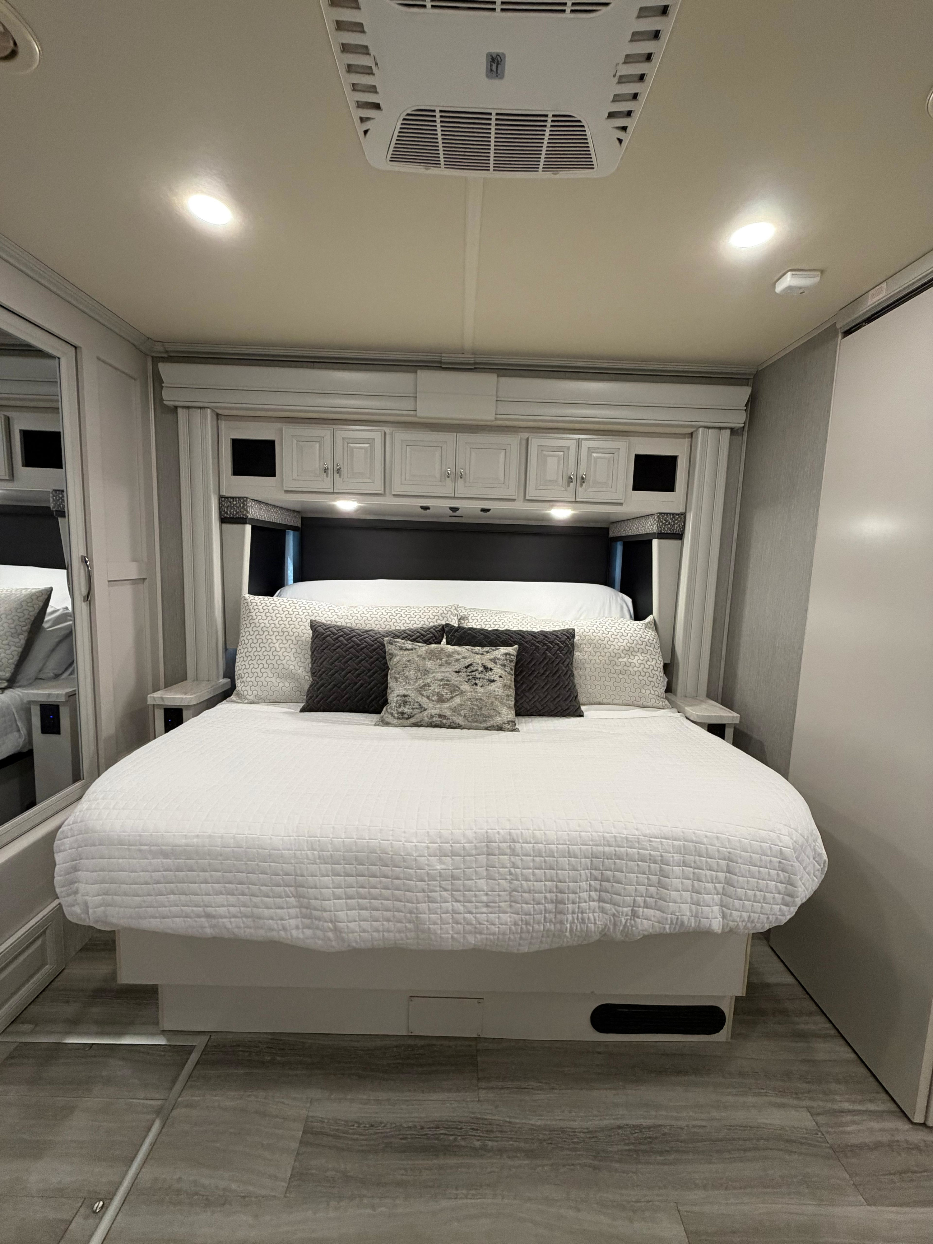 Modern RV rental bedroom with a cozy bed, overhead storage, and a ceiling AC unit, offering comfort for your journey.. Holiday Rambler Nautica 2021