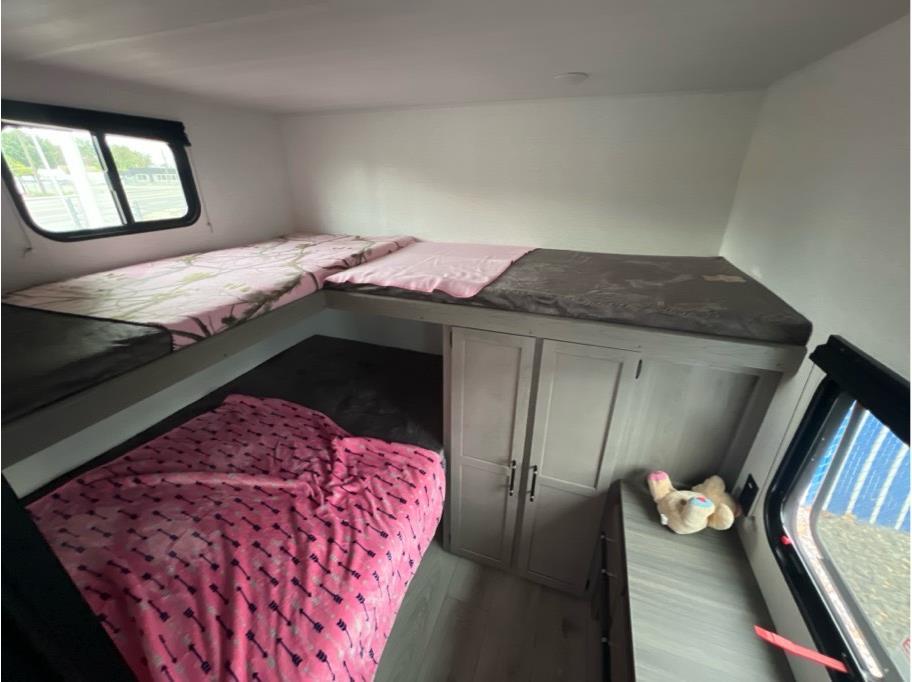 This RV rental bunkhouse features comfy L-shaped bunks with pink accents, lower bed, built-in storage, and windows.. Keystone RV Hideout Sport 2025