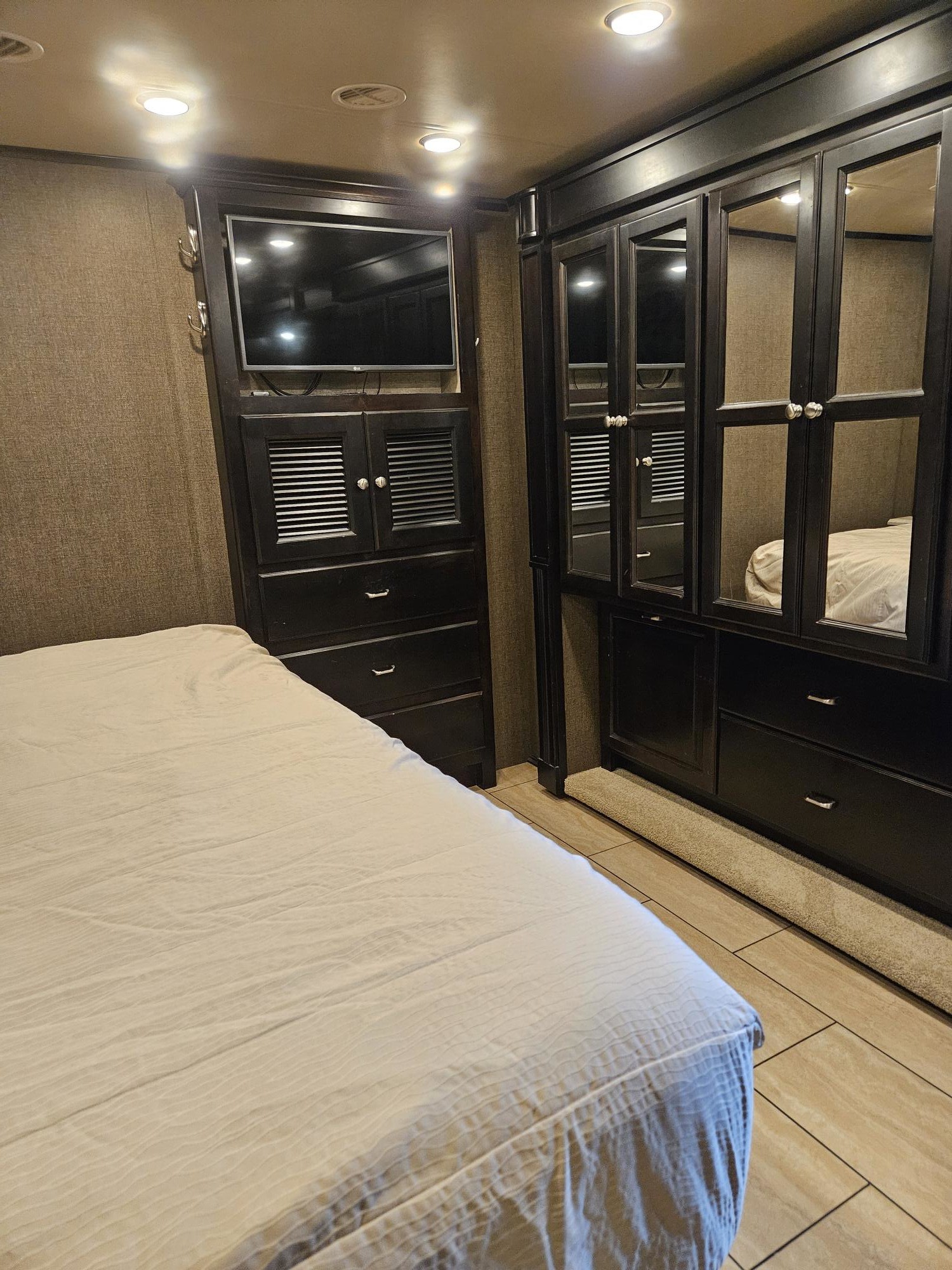 RV rental bedroom: a cozy space with a neatly made bed, TV, dark wood cabinets, and mirrored storage.. Allegro Allegro Open Road 2017